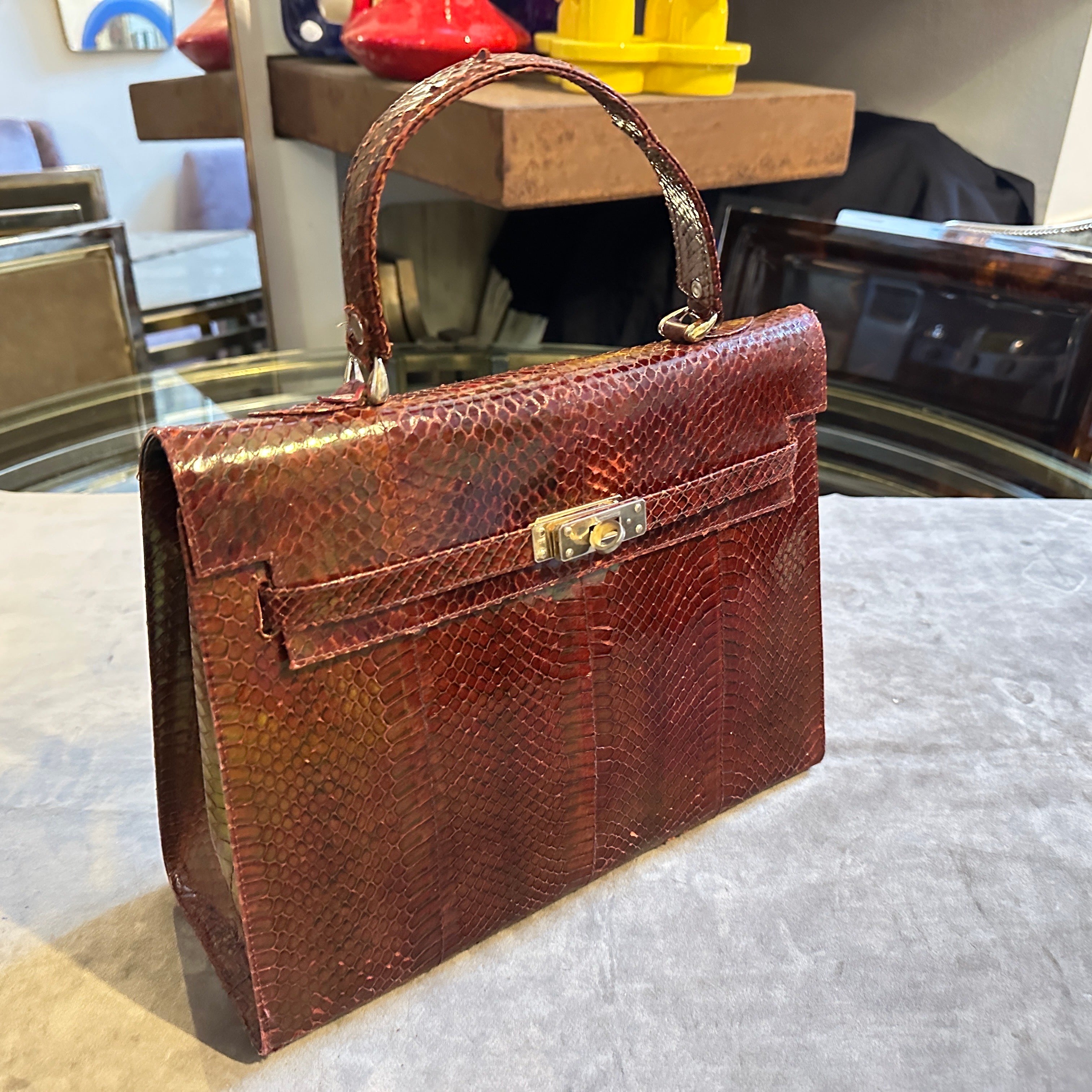 This elegant vintage leather handbag from the 1970s exudes timeless sophistication with its structured silhouette and rich brown leather exterior. Crafted in the manner of Hermès, it showcases a refined sense of style with its sleek top handle and