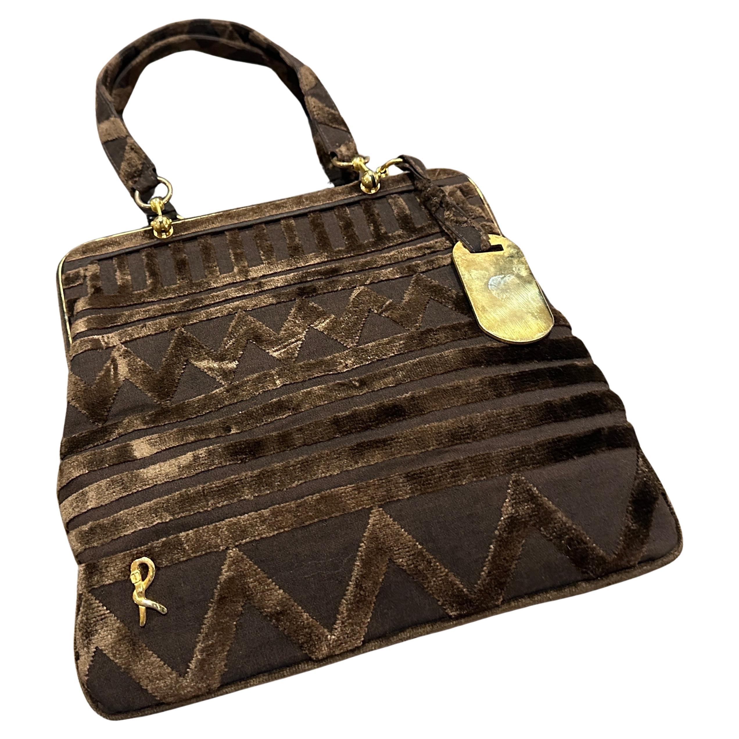 Cet élégant sac à main vintage de **Roberta di Camerne** est un exemple raffiné du design de luxe italien. Confectionné dans un velours **brun** riche et texturé, ce sac présente un motif géométrique frappant qui ajoute de la profondeur et de
