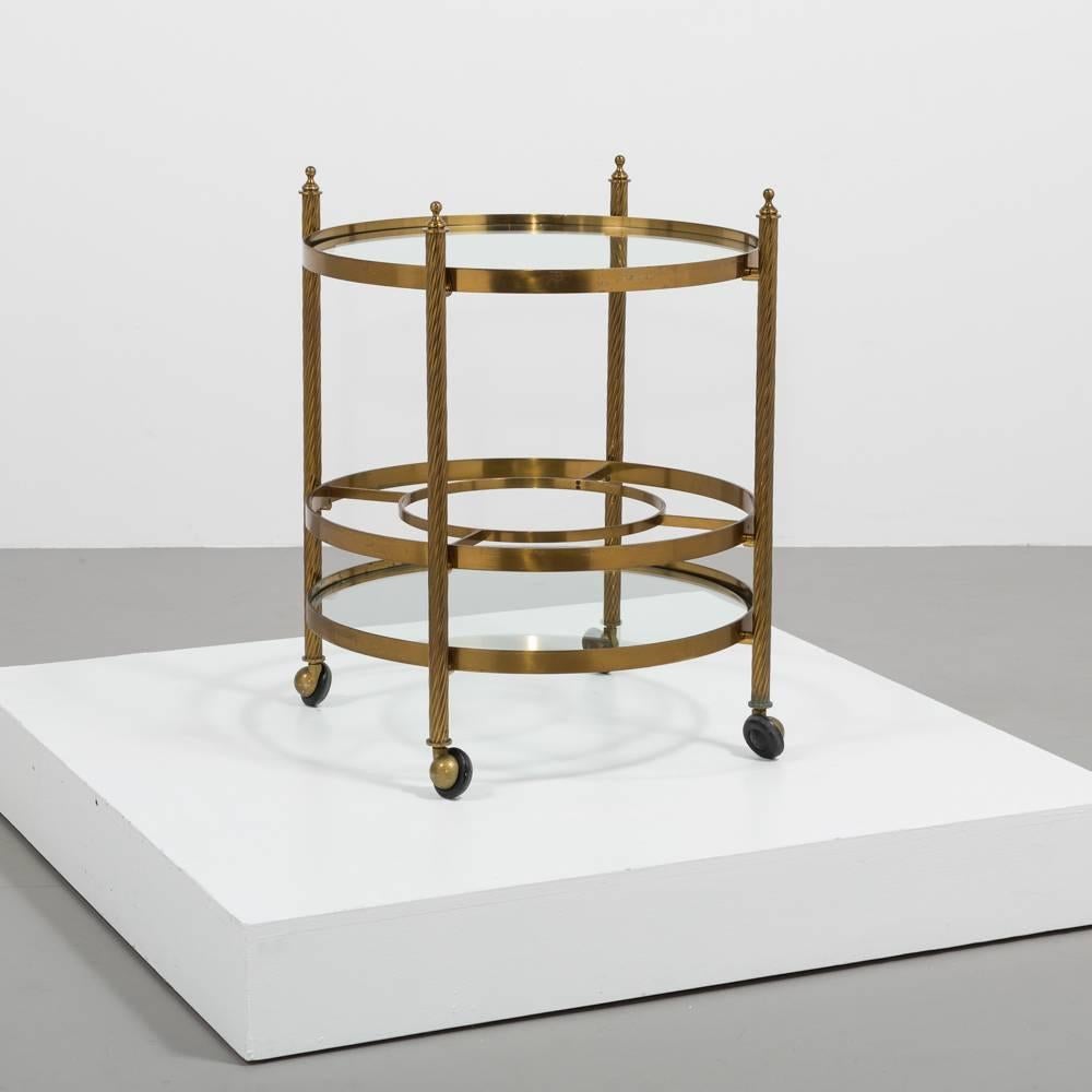An elegant circular brass framed two-tiered barcart on castors with glass shelves and bottle storage detail on the lower tier 1960s.