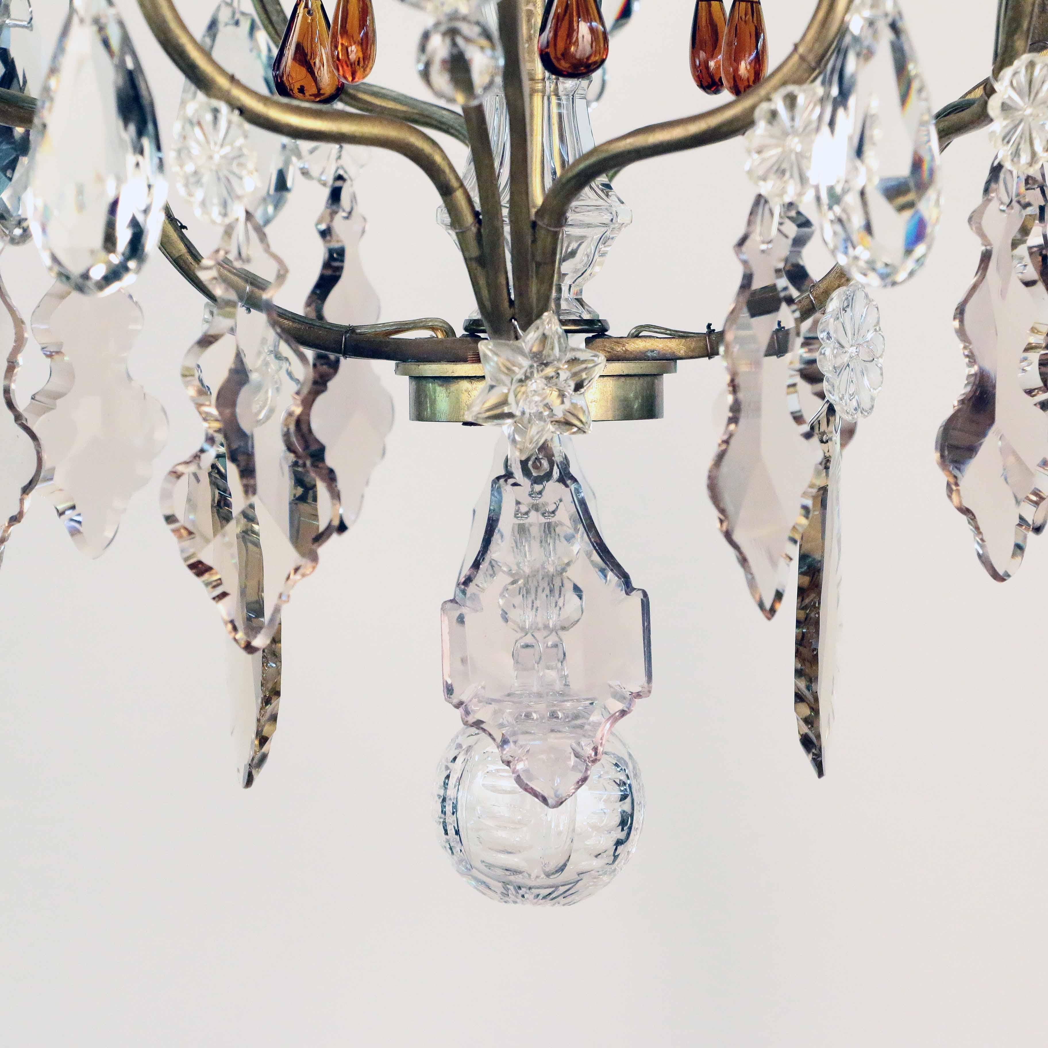 This fixture has a number of unusual qualities. The arms are pierced and bifurcated which adds a sense of lightness. It is decorated with various colored crystal pendants. The finials are hand-blown bulbous spires. The overall effect is light and