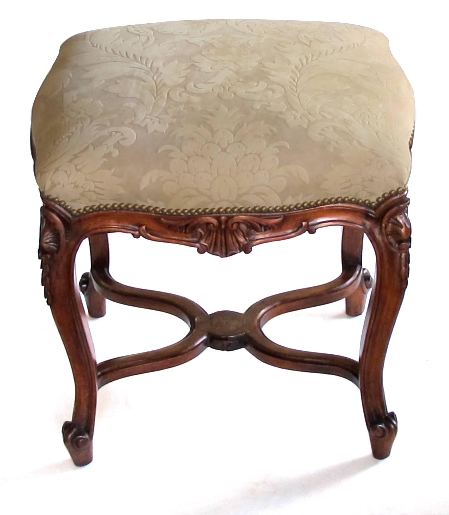 An elegant French Regence style carved walnut serpentine-shaped stool with cut-suede upholstery; the serpentine upholstered seat of new cut-suede upholstery above a shaped apron centering a carved shell motif; raised on cabriole legs with rocaille