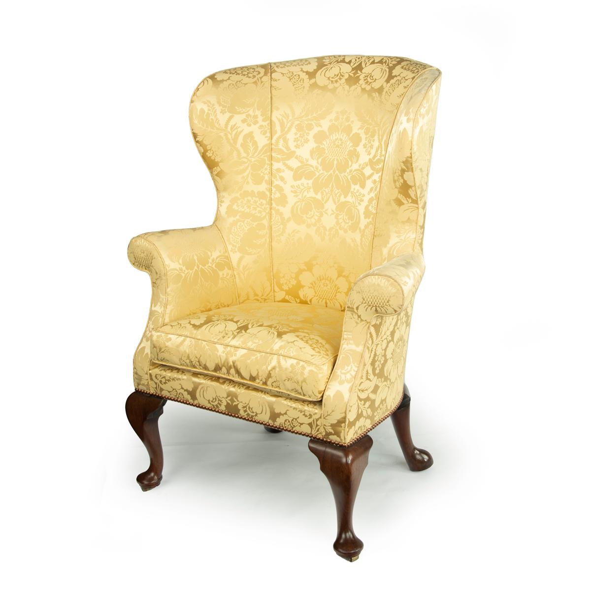 An elegant George I walnut wing armchair, the high barrel back with shallow curving wings and scroll arms, the shallow seat set on four swept cabriole legs with barrel castors enclosed in the pad feet, reupholstered in yellow silk damask. English