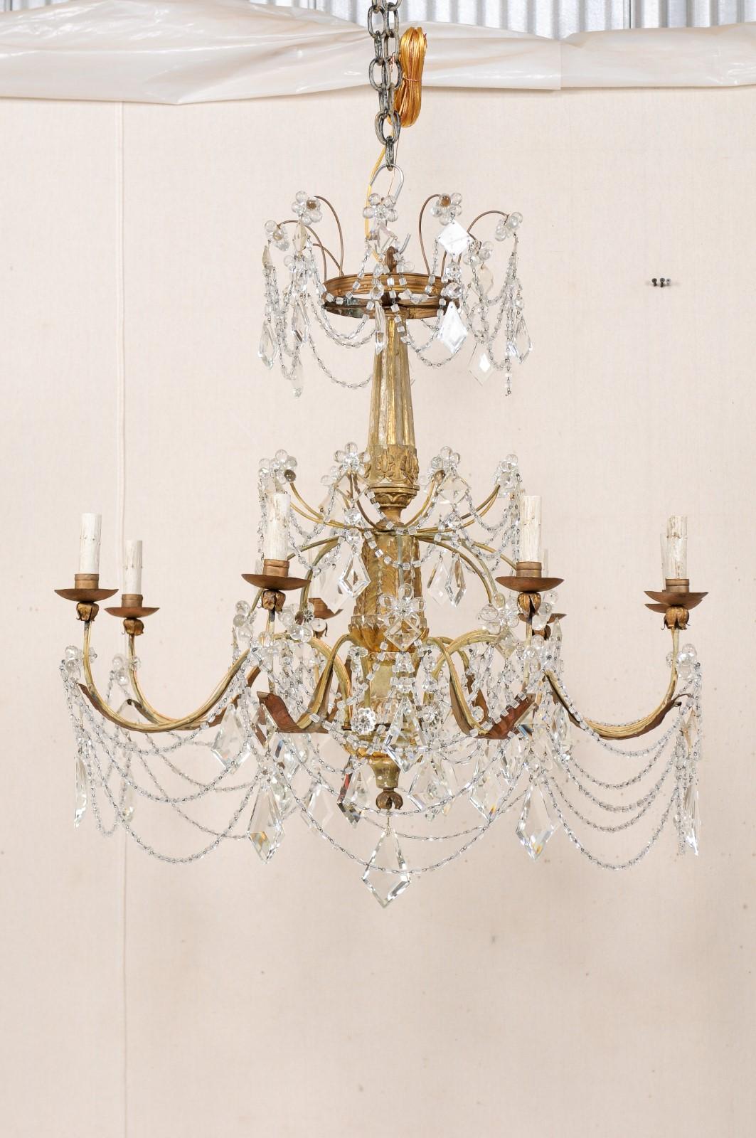 An Italian eight-light crystal chandelier with carved and giltwood column from the early 20th century. This elegant antique chandelier from Italy, which retains its original crystals and gilt finish, features a central wood column carved in a