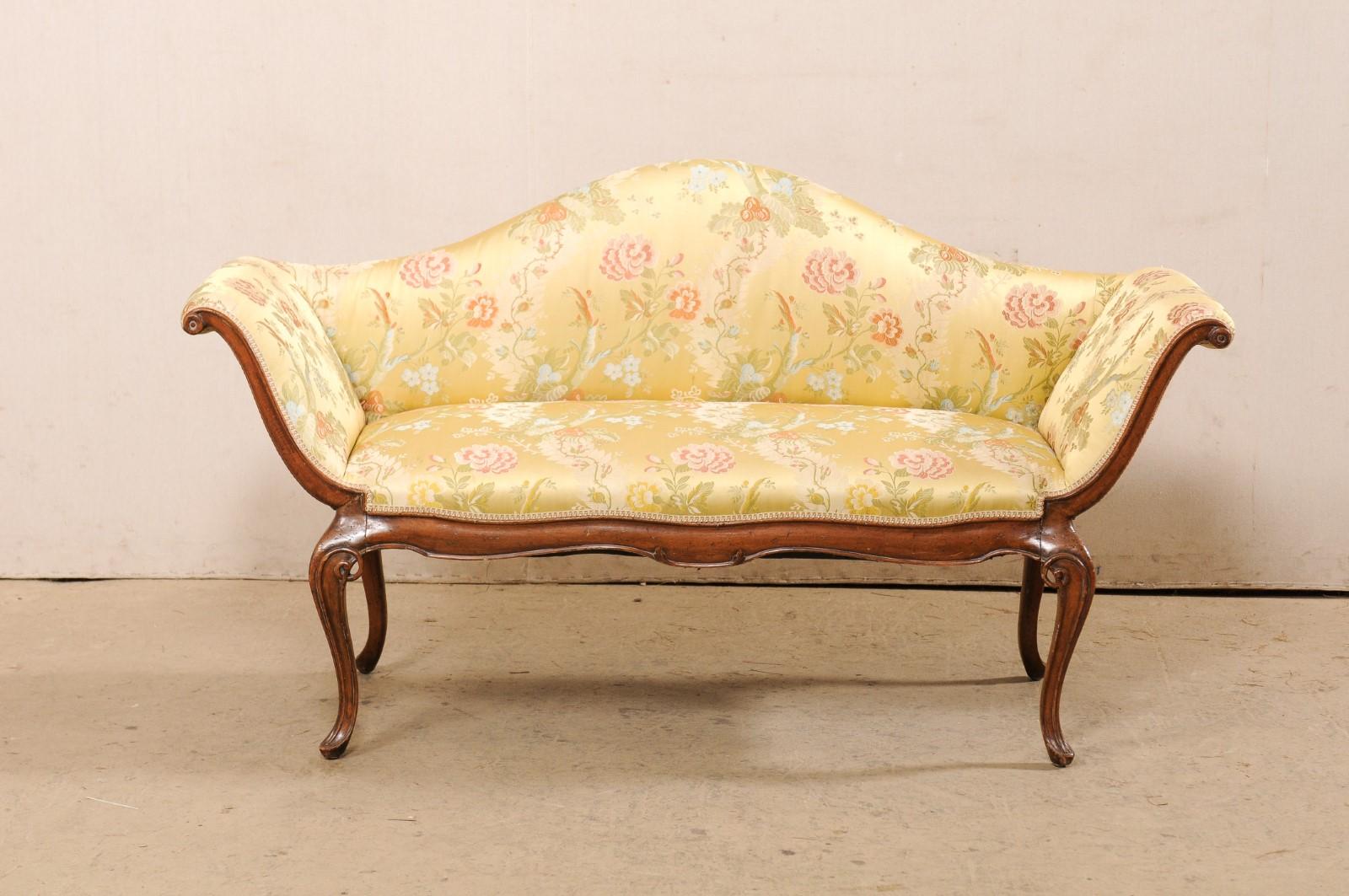 An Italian Venetian style carved wood & upholstered sofa from the early 19th century. This antique settee from Italy features an elegantly arched camel back with gracefully outward tilting arms. Delicately carved wood trim lines the front side of