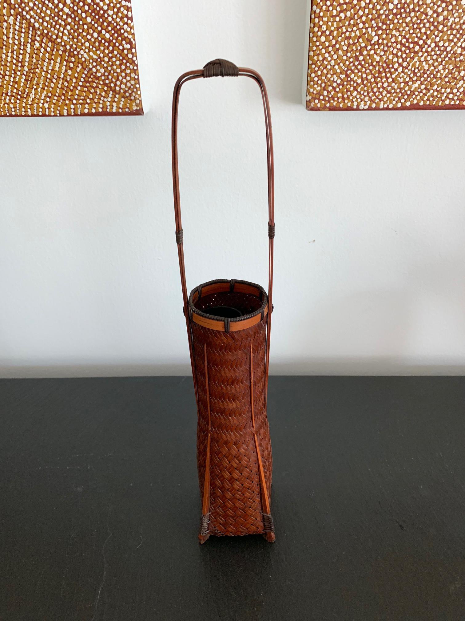 A vintage Japanese ikebana made from lacquered bamboo basketry circa first half of the 20th century. This piece of bamboo art displays an very light and delicate classic tapered square form with tall handle. The artist used split bamboo culms as