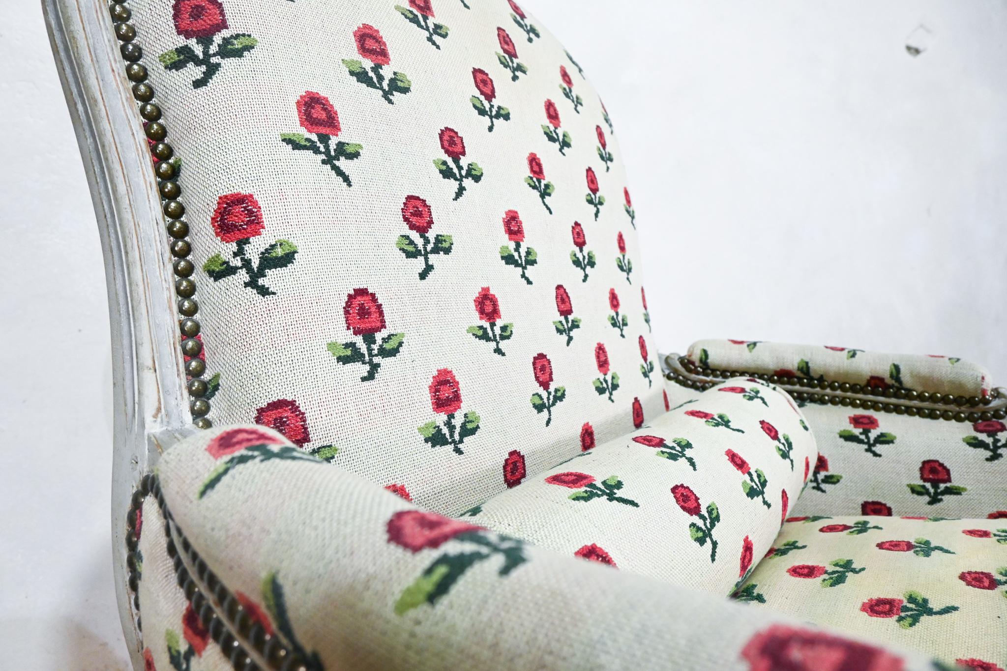 An elegant Louis XV grey painted Bergere by Jean-Baptiste Lebas. Upholstered in a striking period cream fabric, with a subtle green woven undertone, presenting charming red and green floral sprigs. Displaying a cartouche shaped moulded back