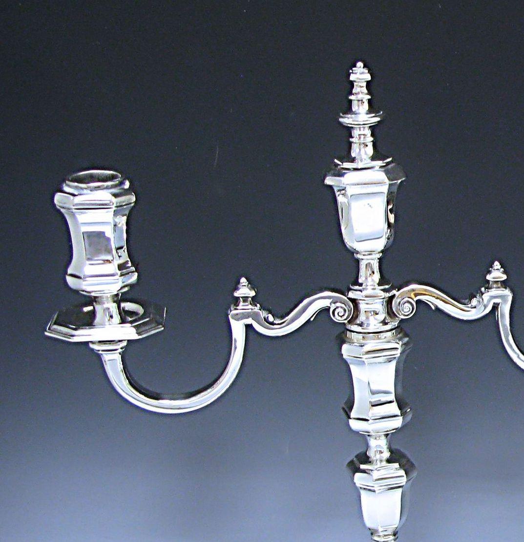 An elegant pair of antique George V cast sterling silver 3-light candelabra, with baluster shaped stems incorporated shaped knops to the upper and lower portions. The candelabra are supported on square stepped bases with cut corners. These