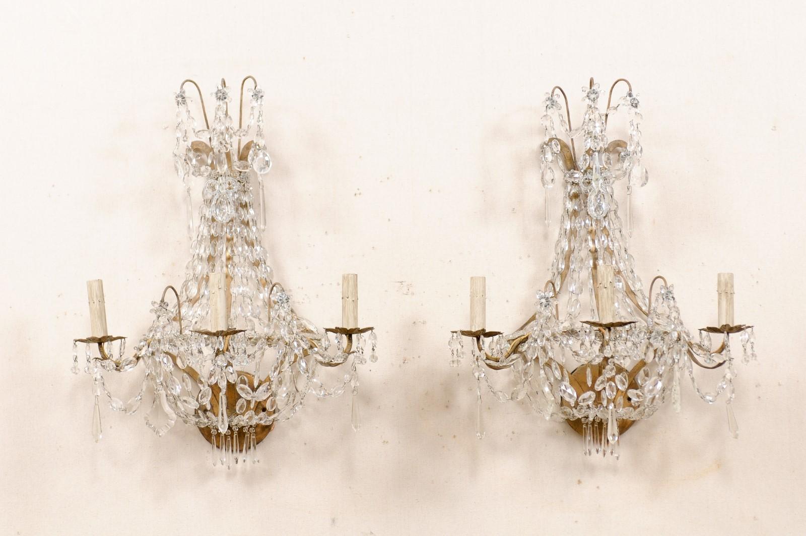 Ein französisches Paar dreiflammiger Wandleuchter aus Kristall aus der Mitte des 20. Dieses Paar Vintage-Wandkandelaber aus Frankreich verfügt jeweils über eine obere, mit Glasblumen und Kristallen verzierte Wasserfallkrone mit darüber liegenden