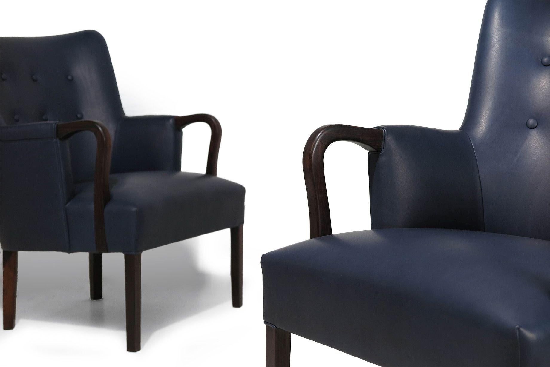 Poltrone finemente scolpite in palissandro brasiliano scuro, attribuite all'architetto danese Kaare Klint, 1939 circa, Danimarca. Queste sedie presentano braccioli elegantemente curvati e gambe affusolate, appena rivestite in morbida pelle blu navy
