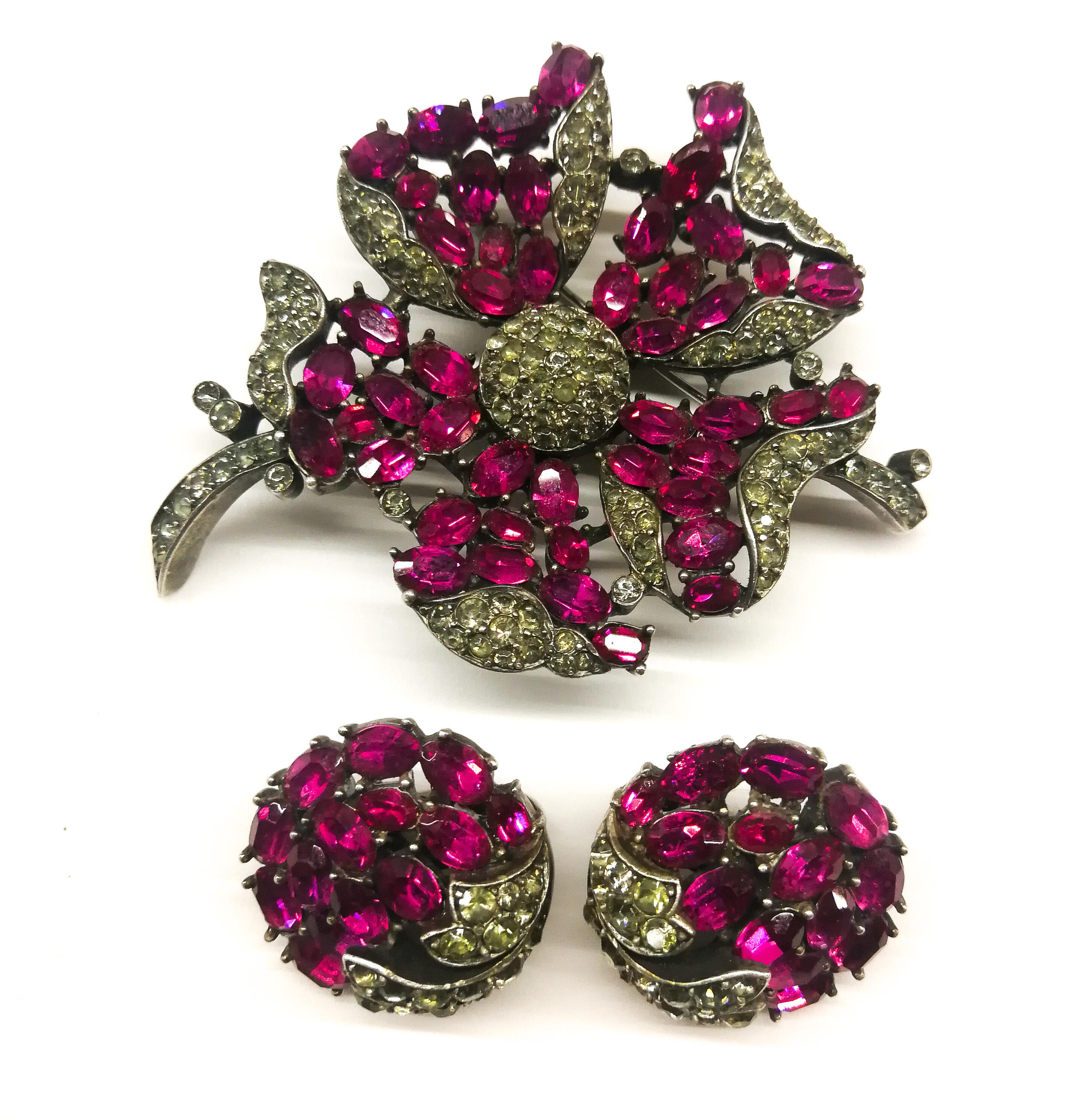 An exquisite brooch and matching earrings, designed by Alfred Philippe for Trifari, made in a sophisticated combination of softest ruby red oval pastes and round grey pastes, set in a burnished silvered metal, in a highly stylised floral design,