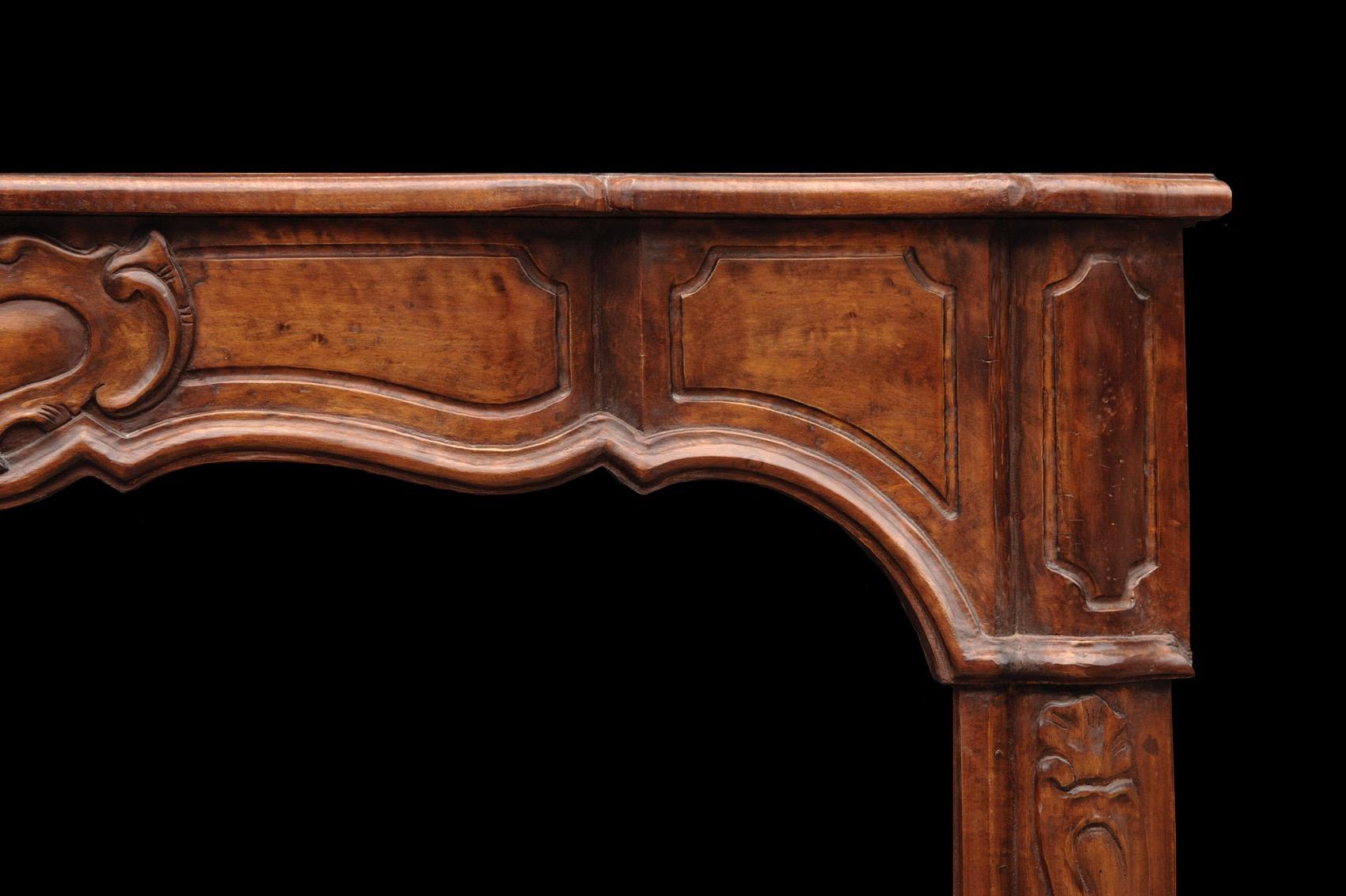 An elegant walnut French Louis XV style fireplace, the centre with carved motif with panelled arbalete frieze, shaped jambs with carved detailing. Shaped serpentine shelf. Early 20th century.

Shelf Width:	1390 mm      	54 ¾