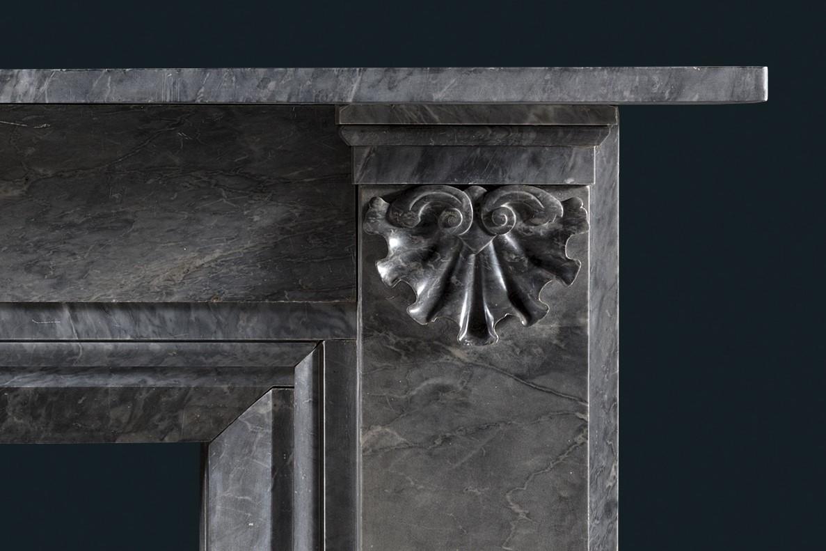 Cheminée du début du XIXe siècle, William IV, en marbre gris Bardiglio, de conception architecturale.
Avec une simple frise de dalles unies et des jambages surmontés de coquilles baroques ornementales. L'ensemble 
élevés sur des blocs.