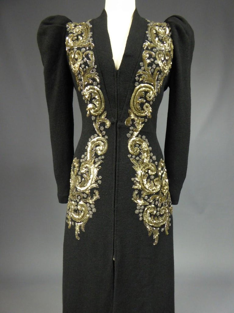 Circa 1938/1940
Paris France

An Elsa Schiaparelli (attributed to) long black woolen coat embroidered by the Maison Lesage with large baroque volute patterns from the shoulders to the hips. Embroideries of mercurised lying fish scales sequins and