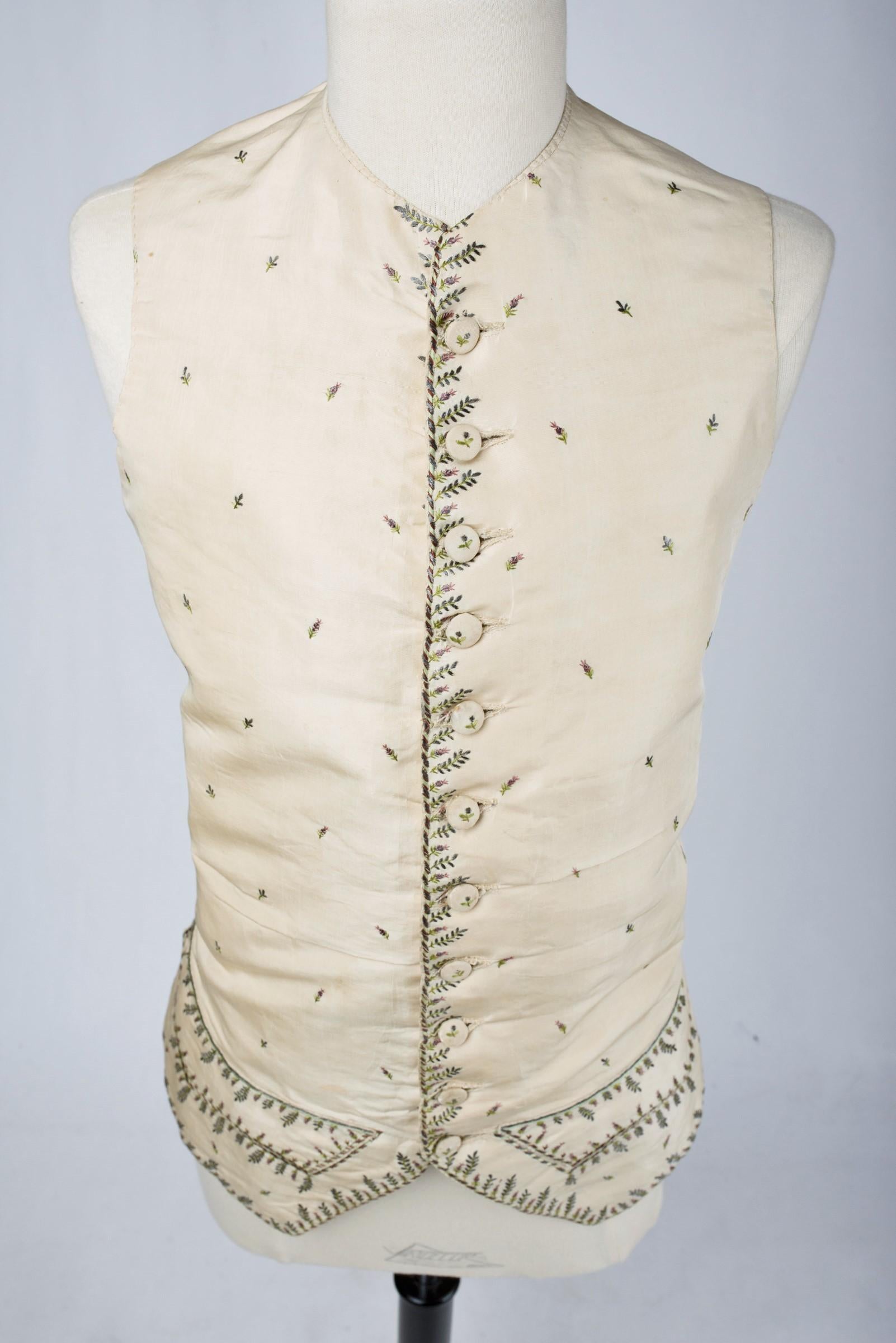 Circa 1785
France

Elegant vest with basques in cream gros de Tours embroidered with silver and polychrome silk threads dating from the Louis XVI period. Embroidery with design of tricolored ribbons on the perimeter dotted with leafy stems, herbs