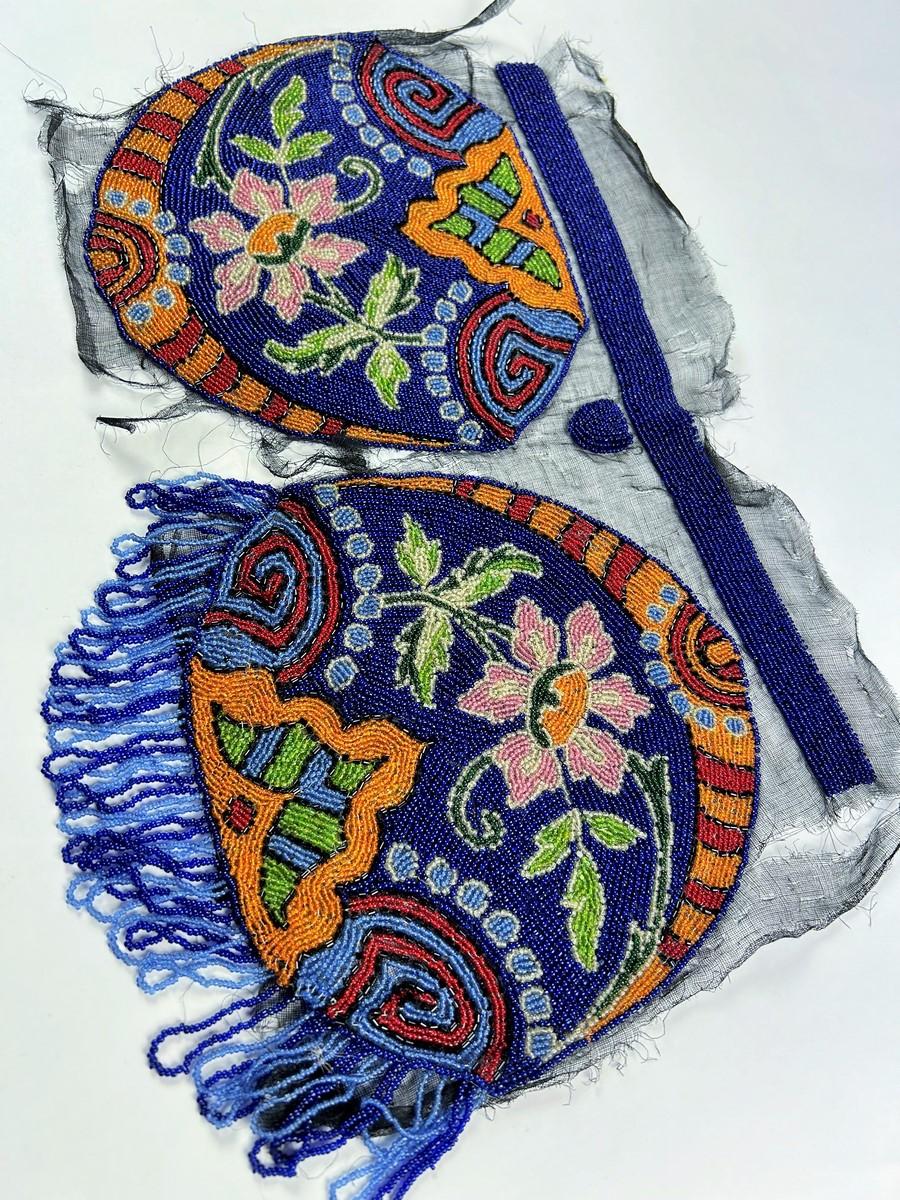 Circa 1925
France
An astonishing Art Deco purse embroidered with polychrome glass beads, said to be ready-made, i.e. before assembly. The embroidery is on a circular black tarlatan tulle, one side of which is fringed. A generous floral design with