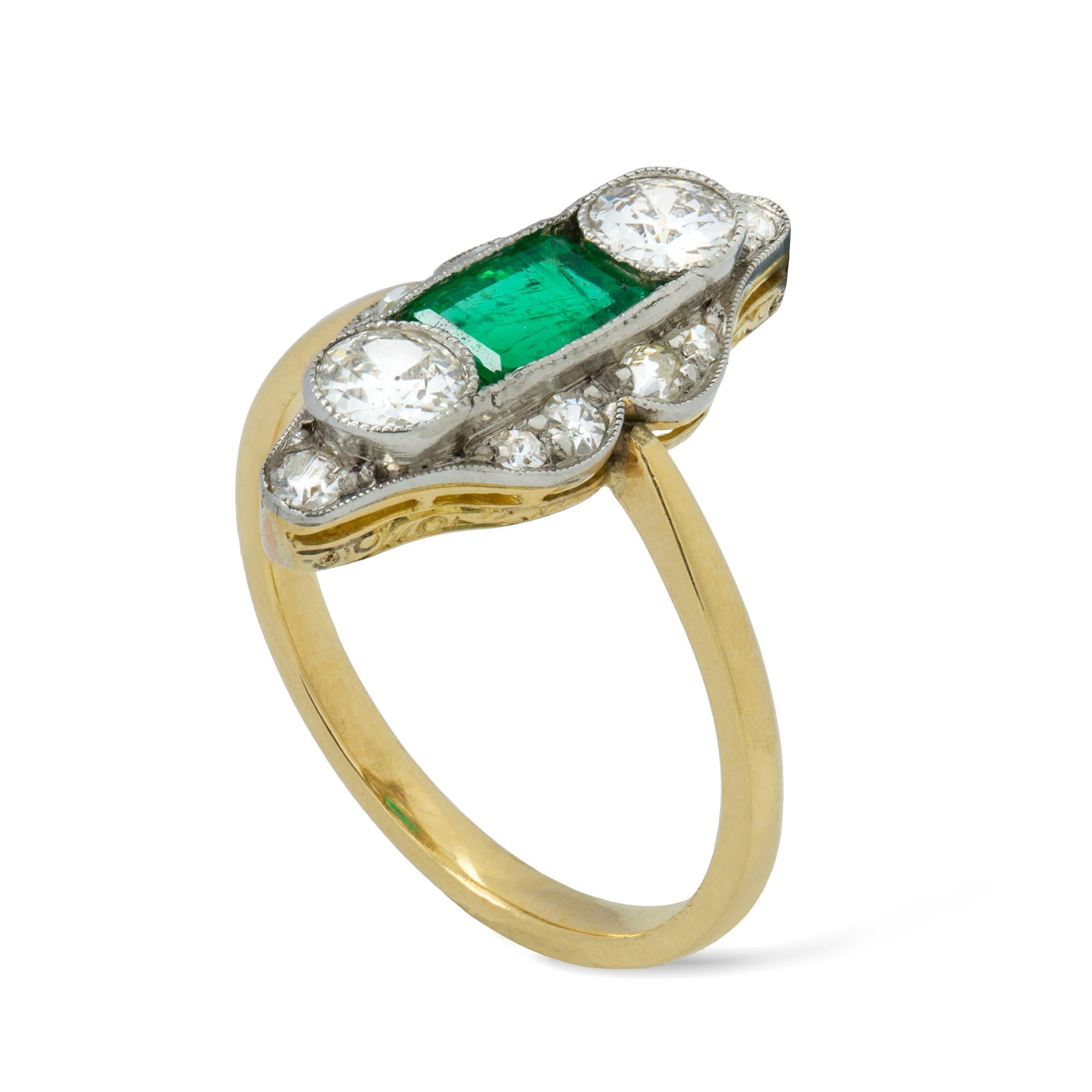 An Edwardian emerald and diamond ring, the rectangular-cut faceted emerald estimated to weigh 0.6 carats and vertically-set between two old European-cut diamonds estimated to weigh ¼ carat each, all surrounded by a navette-shaped frame encrusted