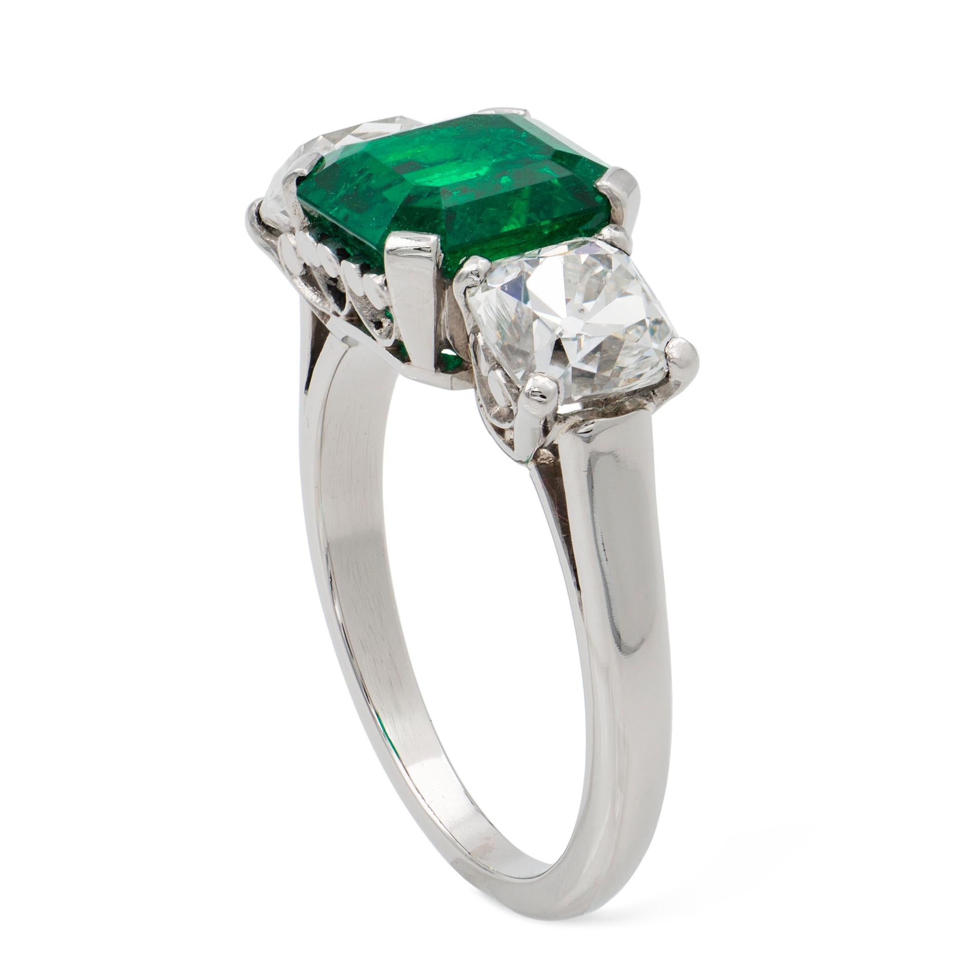 An emerald and diamond three stone ring, the octagonal-cut emerald weighing 2.44 carats accompanied by GCS Report stating to be of Colombian origin, set between two modern Peruzzi-cut diamonds weighing 1.02 and 1.08 carats, all mounted in platinum