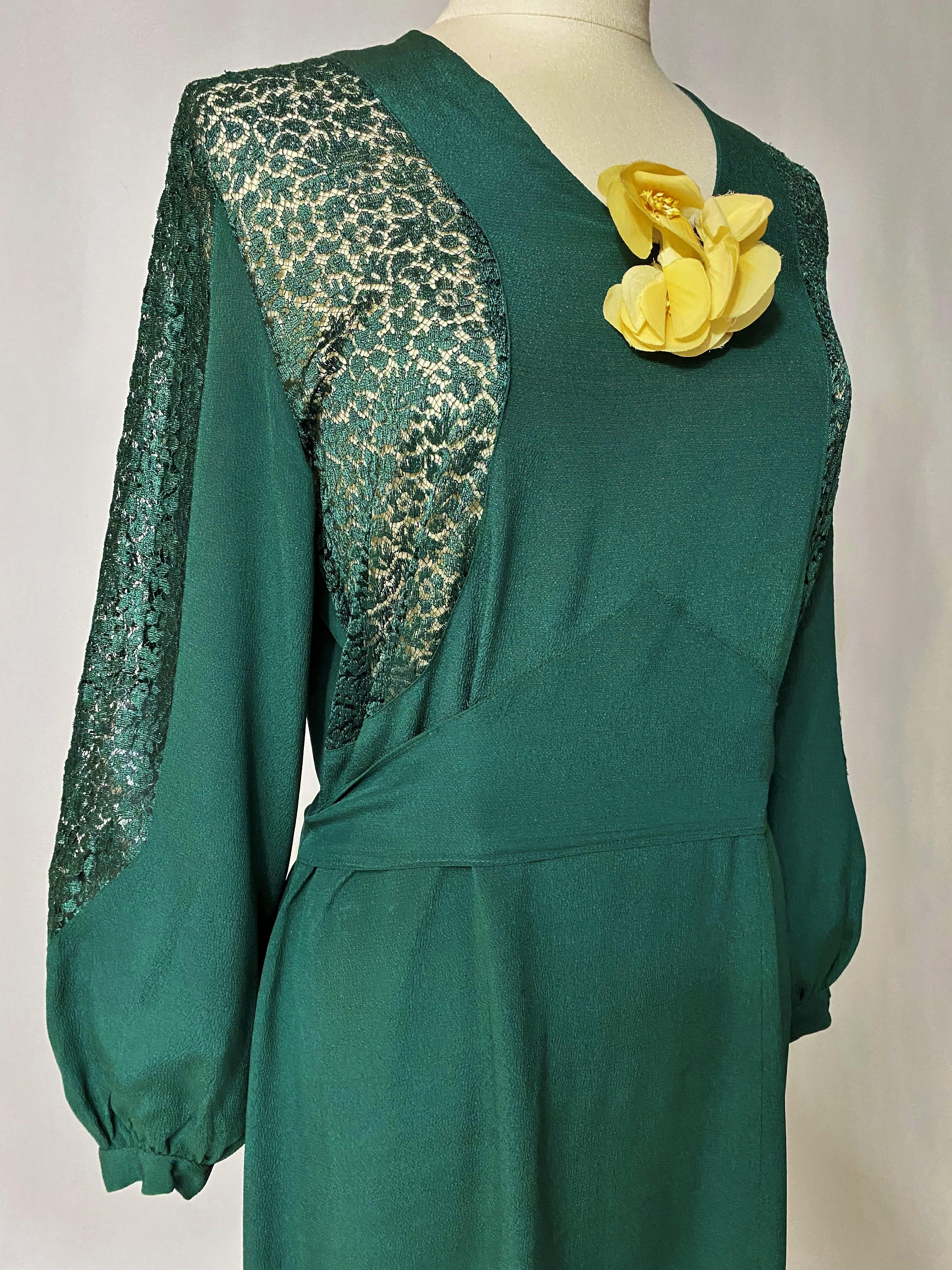 Circa 1935-1945

France

Emerald green crepe evening dress with lace inserts dating from the 1940s. Long dress with puffed sleeves and bib effect. V-shaped applied belt underlines the bustier and is tied behind. Iced cotton flower on the chest (to
