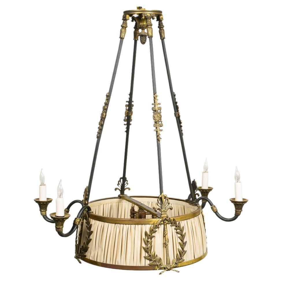 The round flaring shade with ruched silk overlaid with laurel wreaths headed by anthemion and enclosing three lights, issuing four outward scrolling electrified candlearms; suspended by four bronze rods embellised with acanthus clasps joined by a
