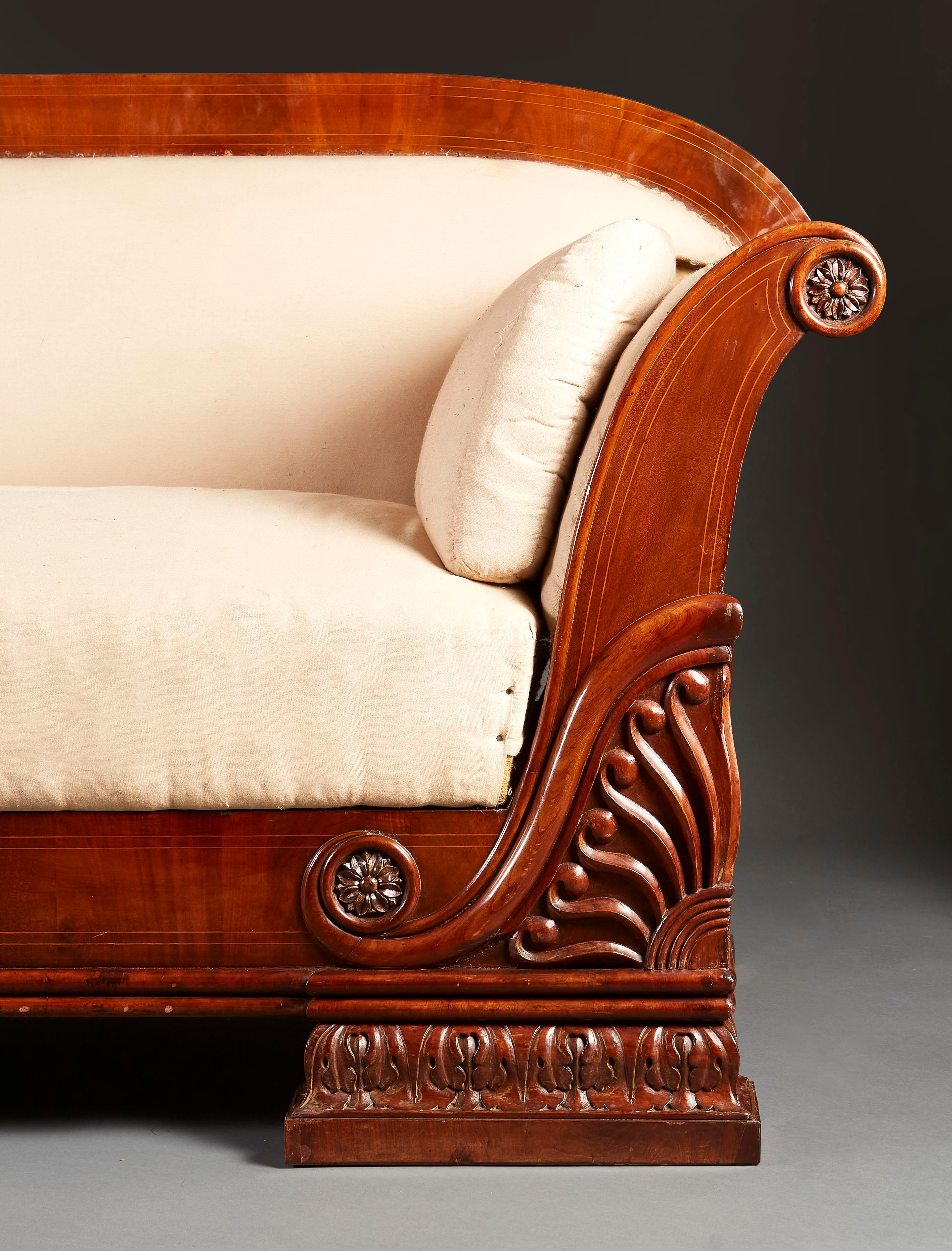 A fine mid nineteenth century Empire sofa, the mahogany frame with unusual carving to the corners and sides, with fans and scrolling decoration, the out swept arms with carved medallions, all supported on bracket feet carved with acanthus leaf motif.