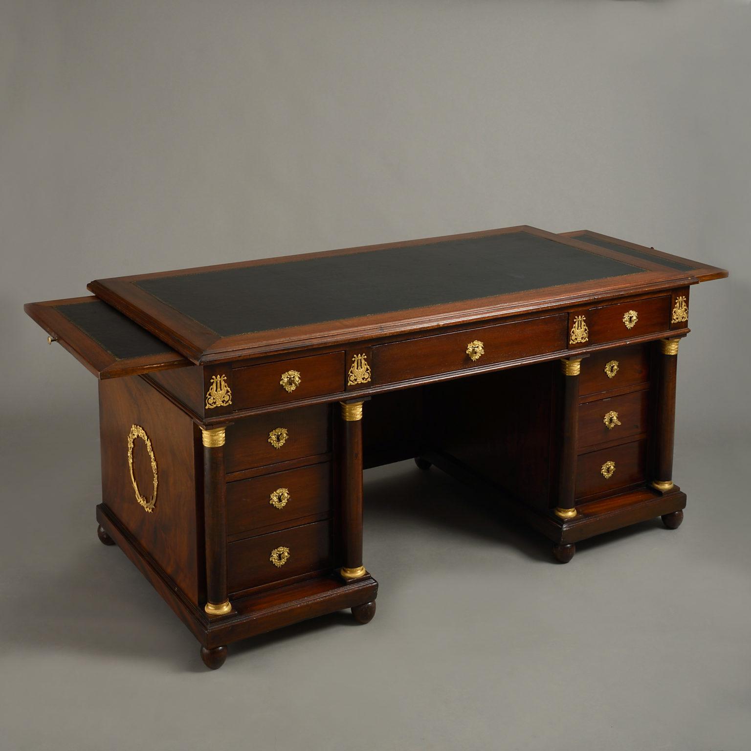 A mid-20th century mahogany desk of good scale, the tooled leather overhanging top with side candle slides of the same and having one long and two short drawers and set upon two plinth supports, each flanked by classical columns with engine turned