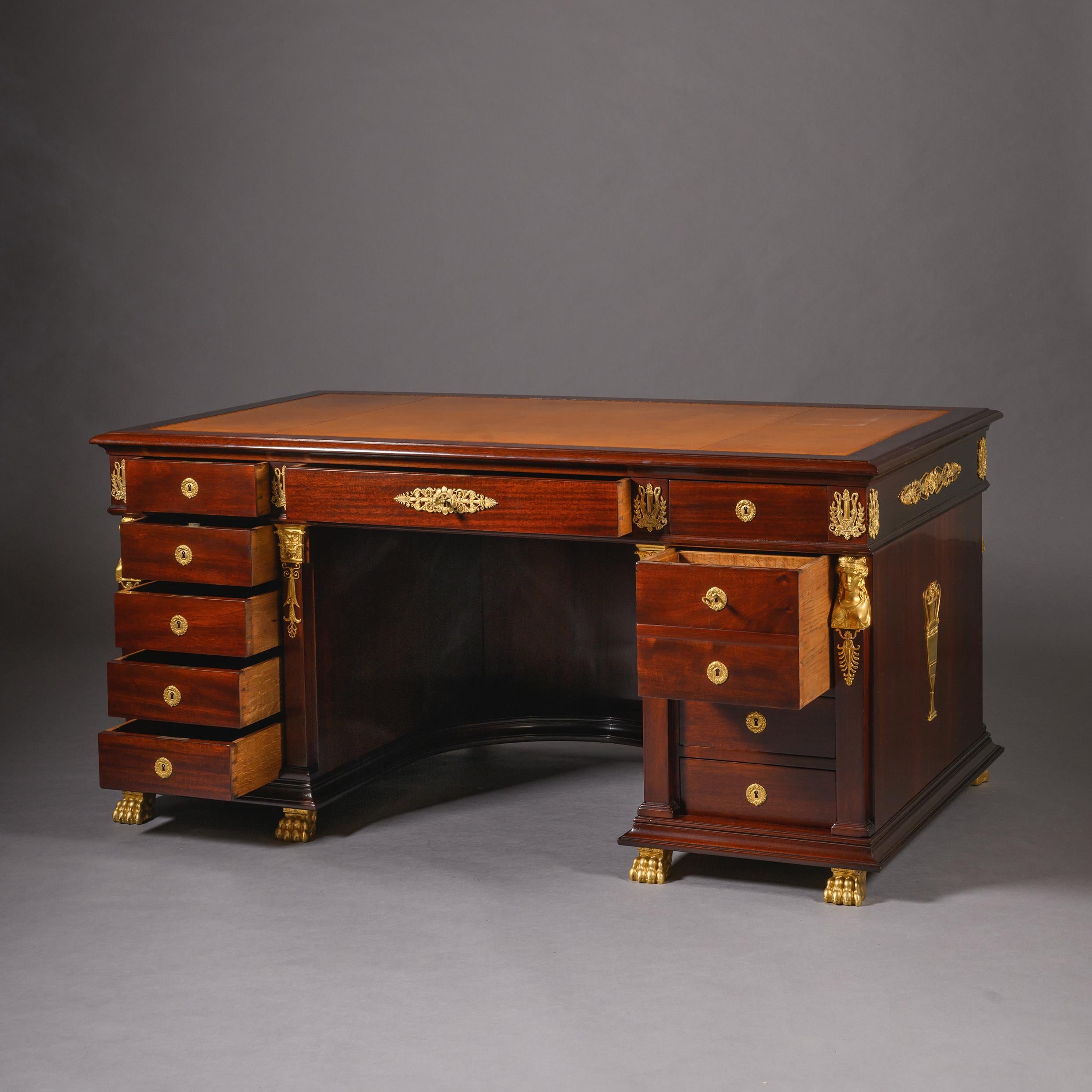Scrivania a piedistallo in mogano con montatura in bronzo dorato in stile Impero, di  Kahn, Parigi.

Il piano rettangolare è dotato di una superficie di scrittura in pelle marrone. Il fregio è preceduto da tre cassetti sopra dei piedistalli che