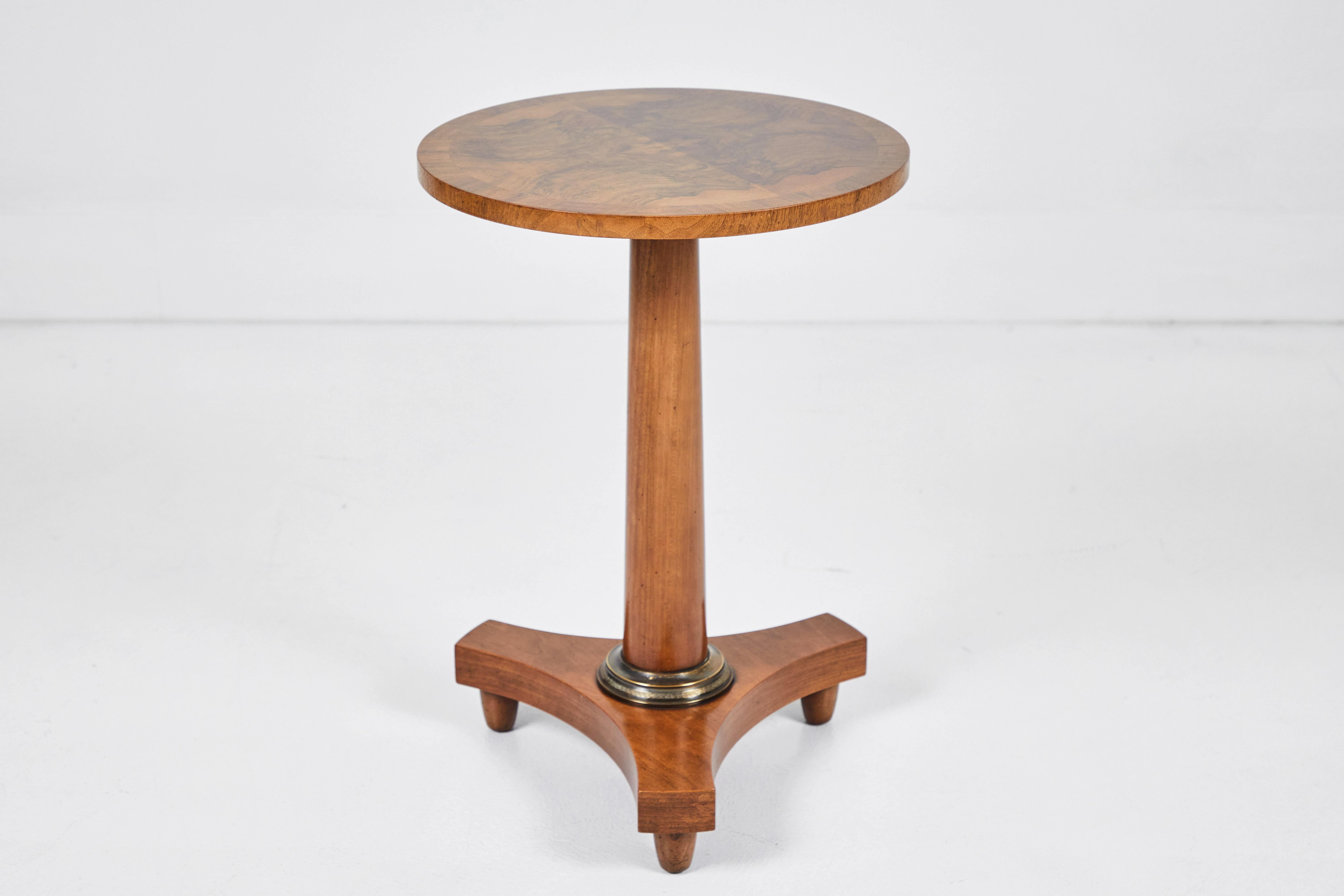 This Baker Empire occasional table is in excellent condition. The grain in the burl wood walnut top is beautiful. The the stem base tapers out just slightly and finishes with a wonderful brass detail. The three legged base extends 5.5