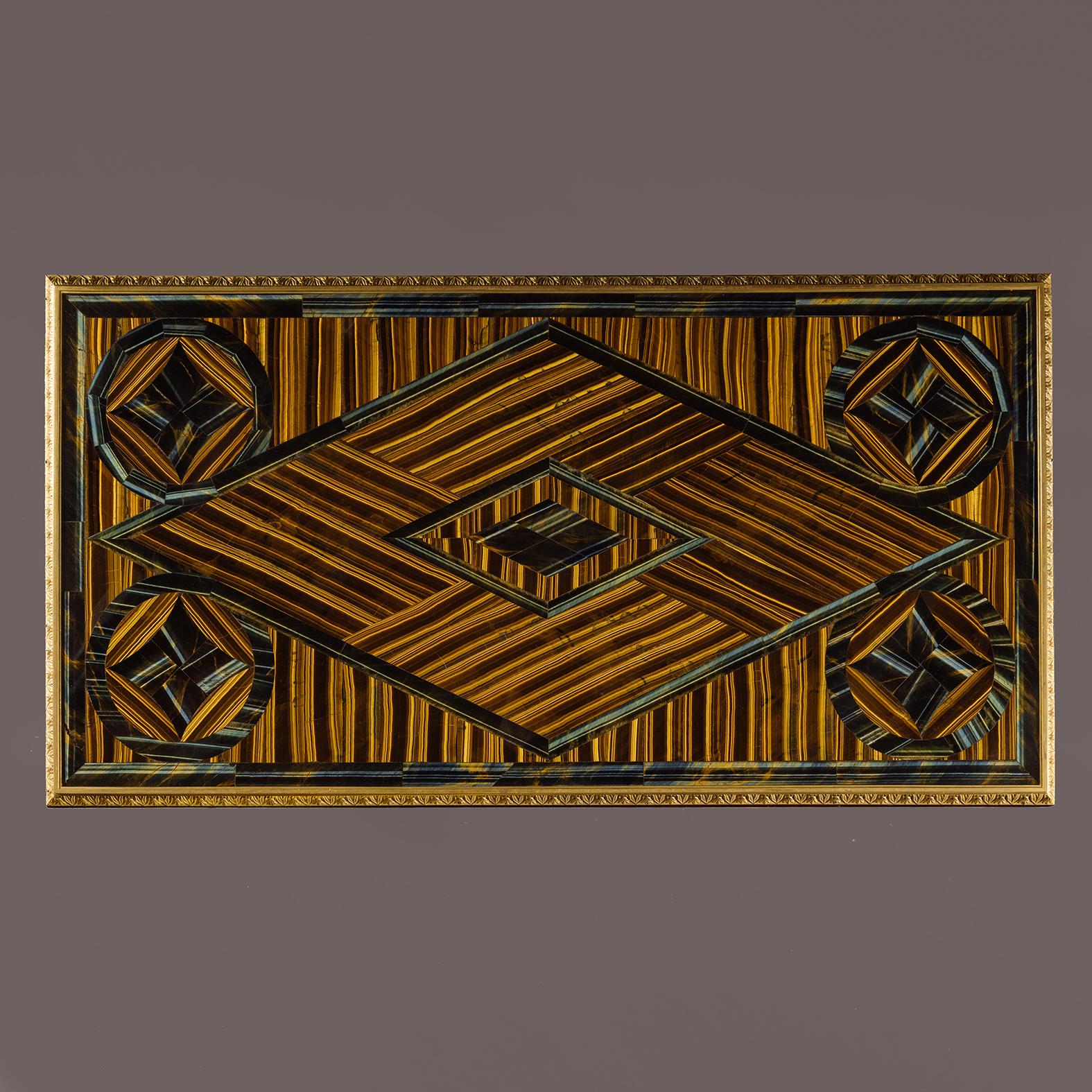Table de salon de style Empire en acajou monté en bronze doré, avec plateau en pierre précieuse œil de tigre.

Le plateau rectangulaire est plaqué de pierres précieuses Œil de tigre en motifs géométriques rayonnants. La frise est montée en bronze