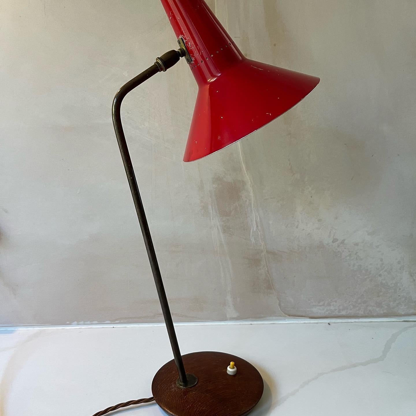 An English 1950’s red enamel and gilt metal desk lamp designed by Beverly Pick for GEC. A lovely example of good British midcentury modern design. Original paint with minor scuffs and paint loss. The brass has a good patination as does the wooden