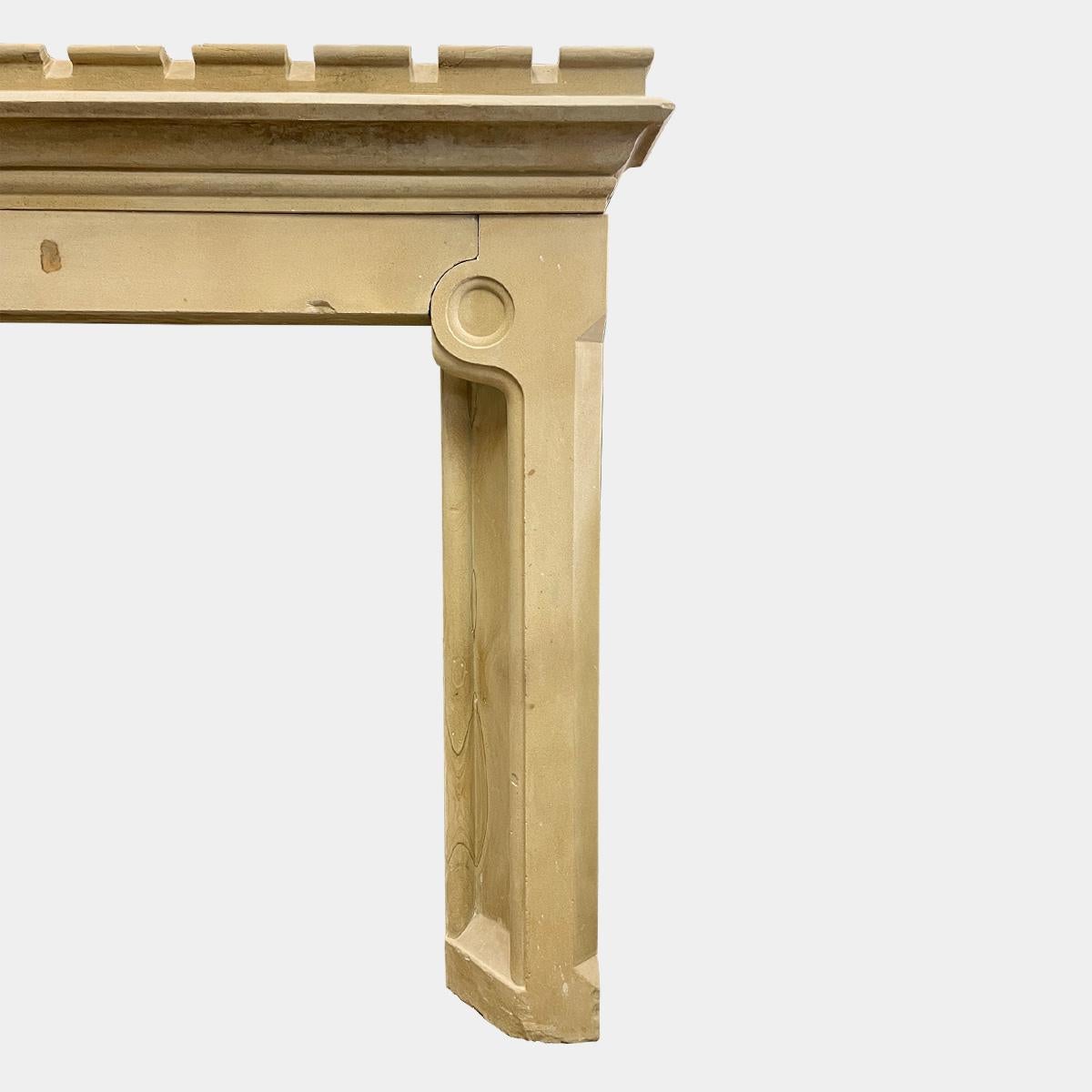 An early to mid 19th century Gothic style English limestone fireplace. Unusual in design, very well proportioned and a substantial piece. The castellated shelf which steps down to sit on a plain frieze with carved ends to meet the roundels carved at