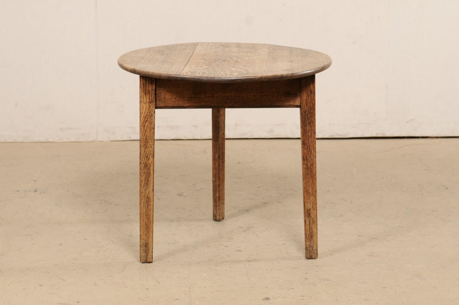 An English round-shaped oak-wood occasional table from the 19th century. This antique center table from England has a round top which overhangs a triangular apron below, and is raised on three triangular legs. Please note that the oak top is more