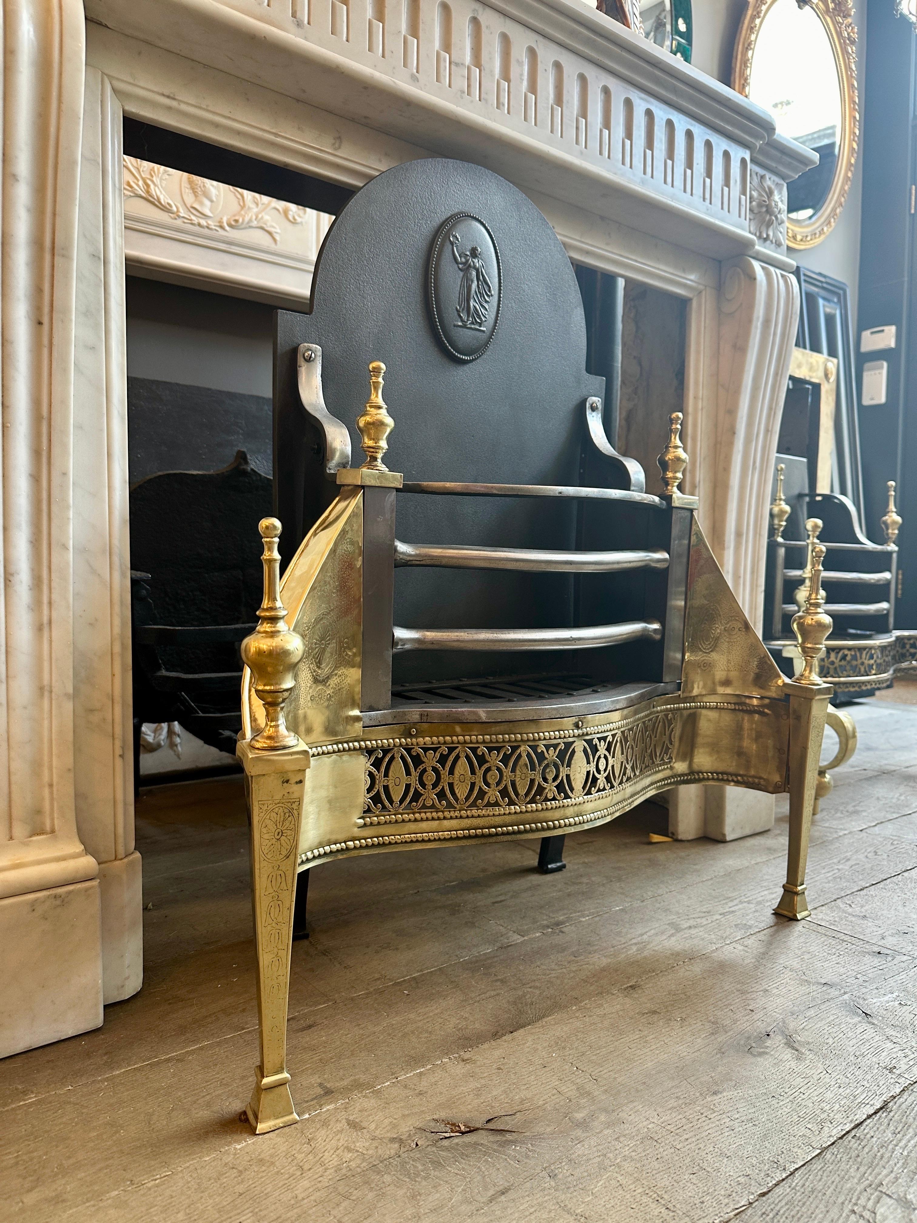 An unusual English Mid 19th century fire grate in the earlier Georgian manner.  The tall shaped original fireback decorated with a classical female figure medallion with beaded edge. The tapering front pedestal legs with engraved fronts and