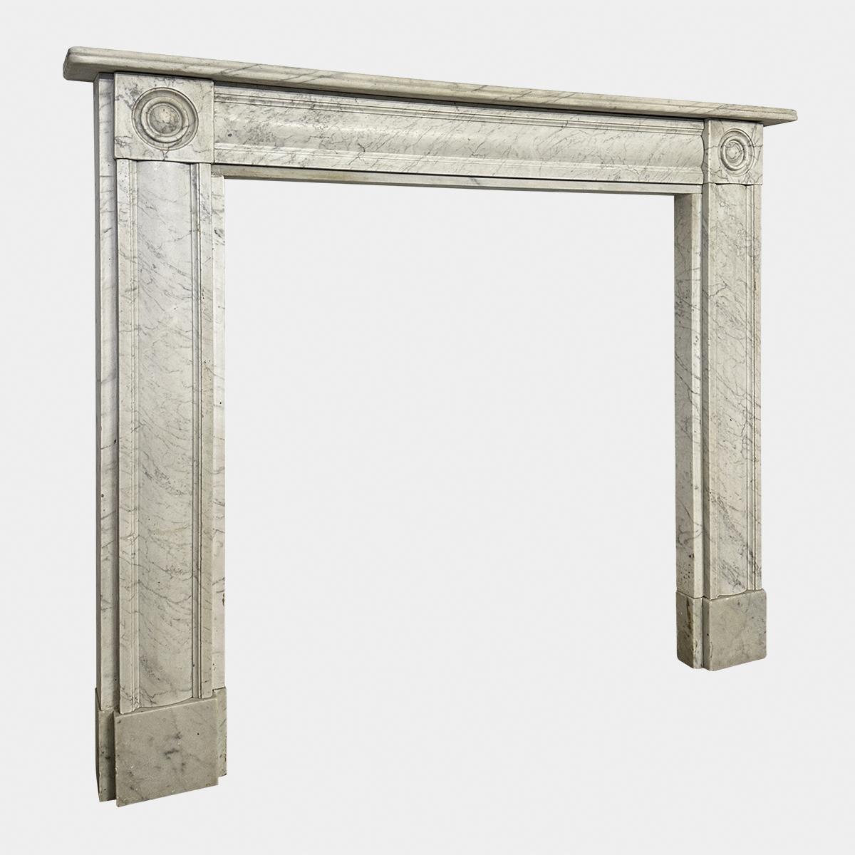 An English Regency period Fireplace executed in Italian Carrara marble. A very good example of this style of surround, The jambs stood on square foot blocks with a wide cushion moulding terminating in carve roundel 