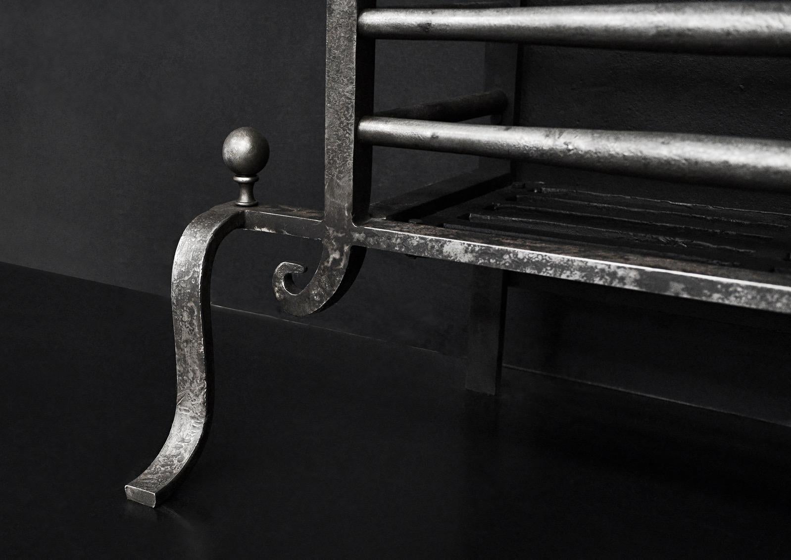 An English antique steel firegrate. The shaped feet surmounted by ball finial, the burning area with elegant front bars and shepherd's crook finials on each side. Square cast iron fireback. A copy of an original piece. N.B. May be subject to an