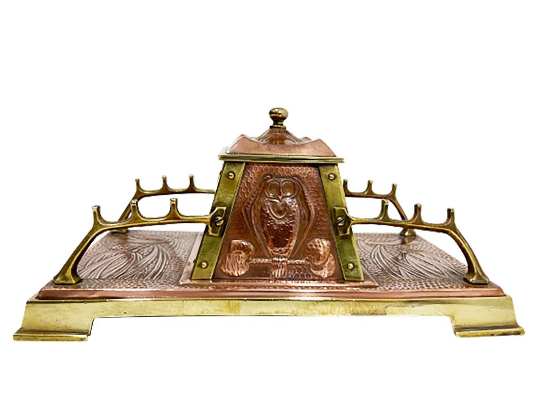 An English Art Nouveau copper inkwell. 

An Art & Crafts English yellow with red copper inkwell. A rectangular inkwell with a scene of an owl sitting on a branch on each side of the inkwell and floral decor, hammered and nailed by hand. There are