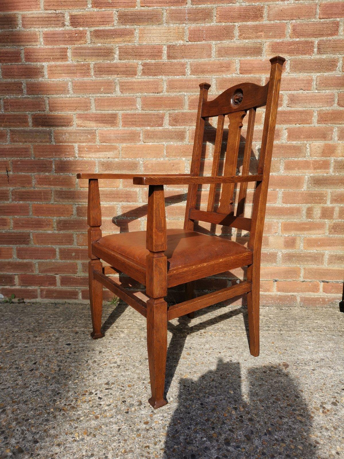 An English Arts & Crafts oak armchair with a carved Mouse inset to the headrest flanked by extended capped uprights with a shaped central back spat and a drop in brown leather seat with incised details around the front legs above and below the seat,