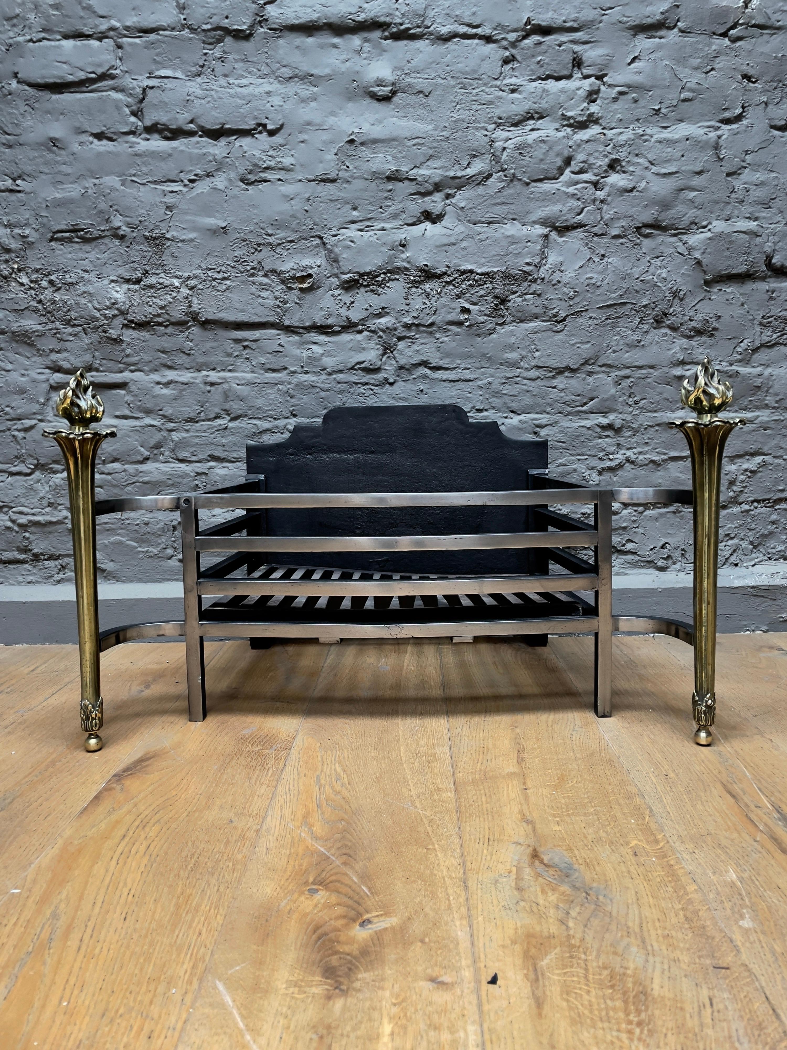 A wide and elegantly designed fire grate in polished steel with brass torchère supports and shaped cast iron fire back. 

English, early 20th century.