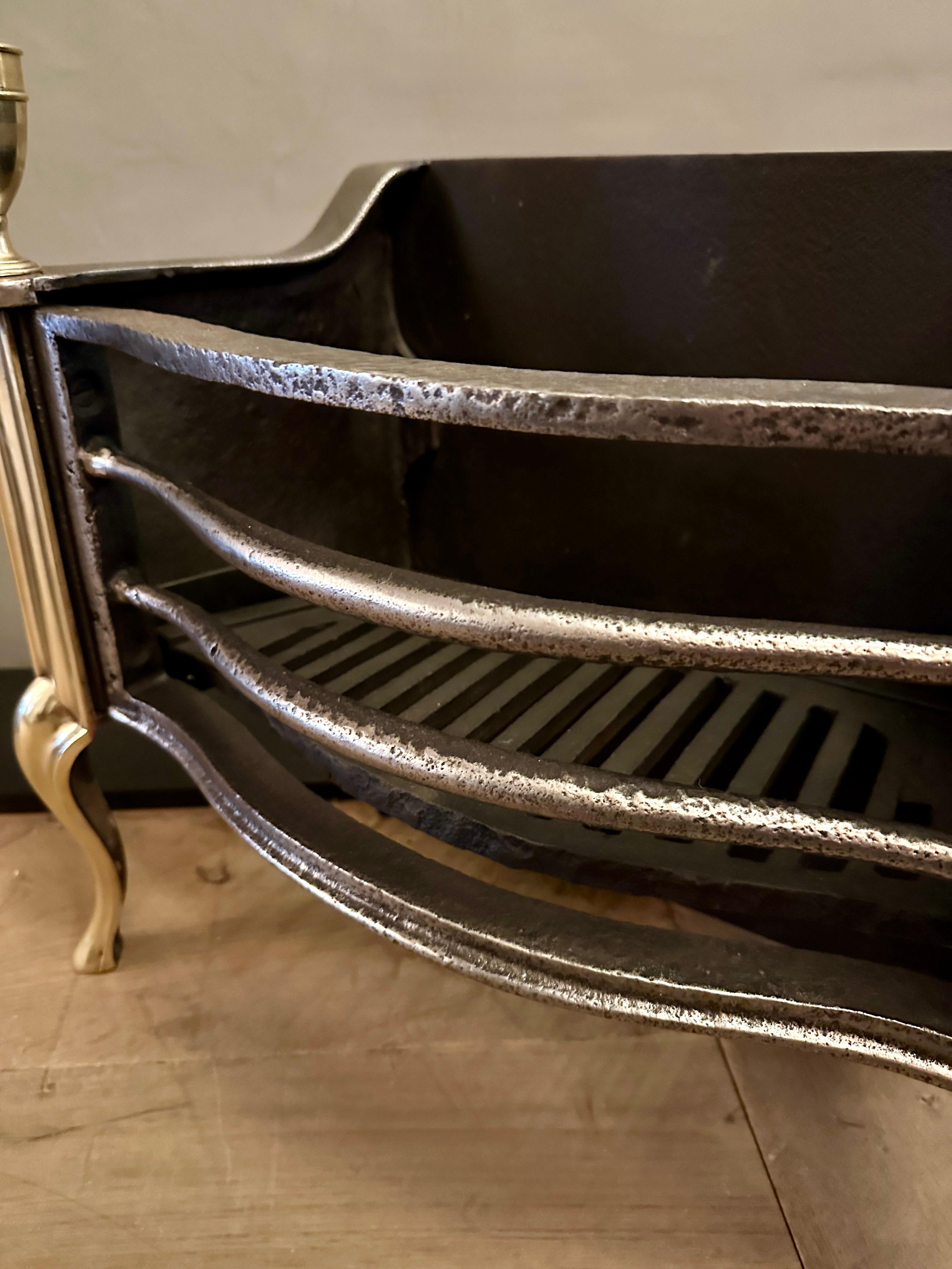 Un antico caminetto inglese in stile Regency in ottone e ferro battuto di Thomas Elsley. Le barre ad arco sono affiancate ai lati da gambe cabriole in ottone e sormontate da grandi urne classiche con finial. Una griglia per il fuoco semplice ma