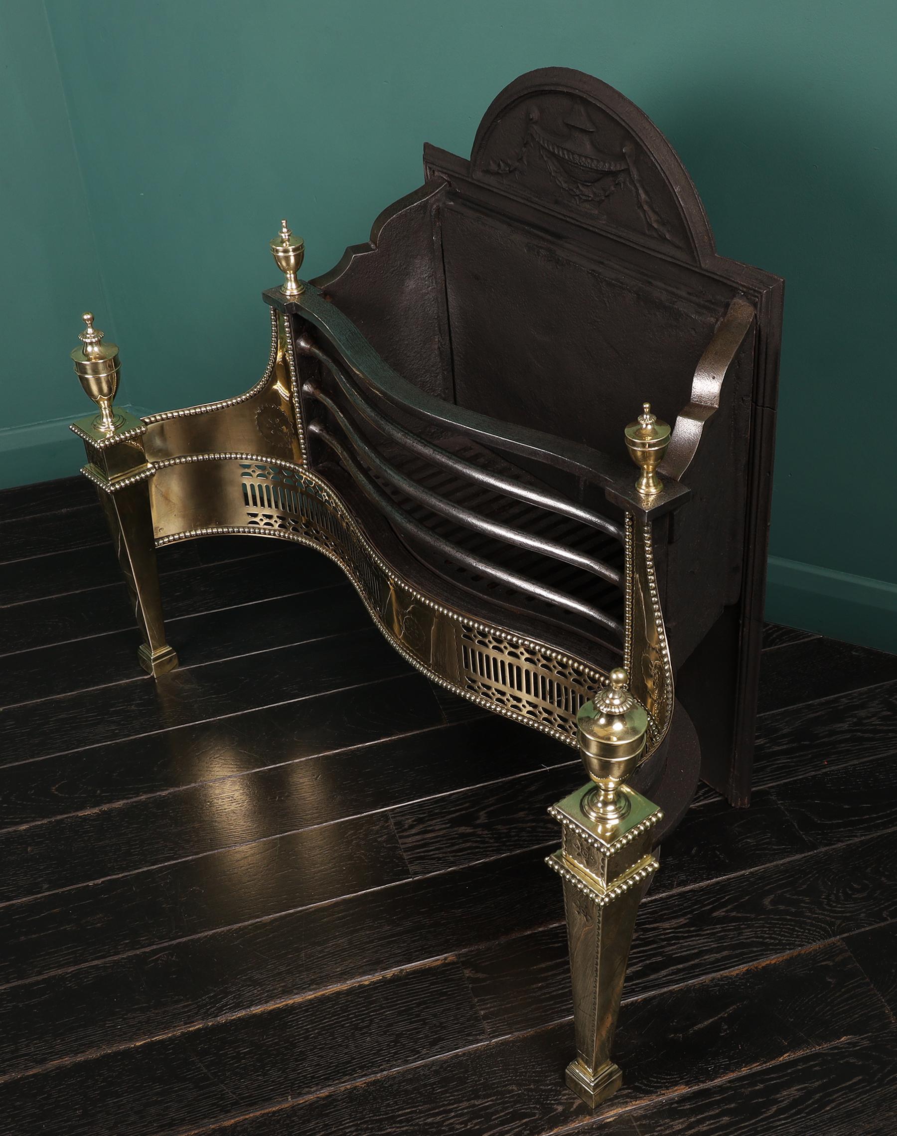 An English brass, polished steel & cast iron fire grate by Thomas Elsley. The railed serpentine basket above a fluted fret set between tapering uprights with urn finials. fine engraving to fret, wings and legs with an arched decorative fire back.