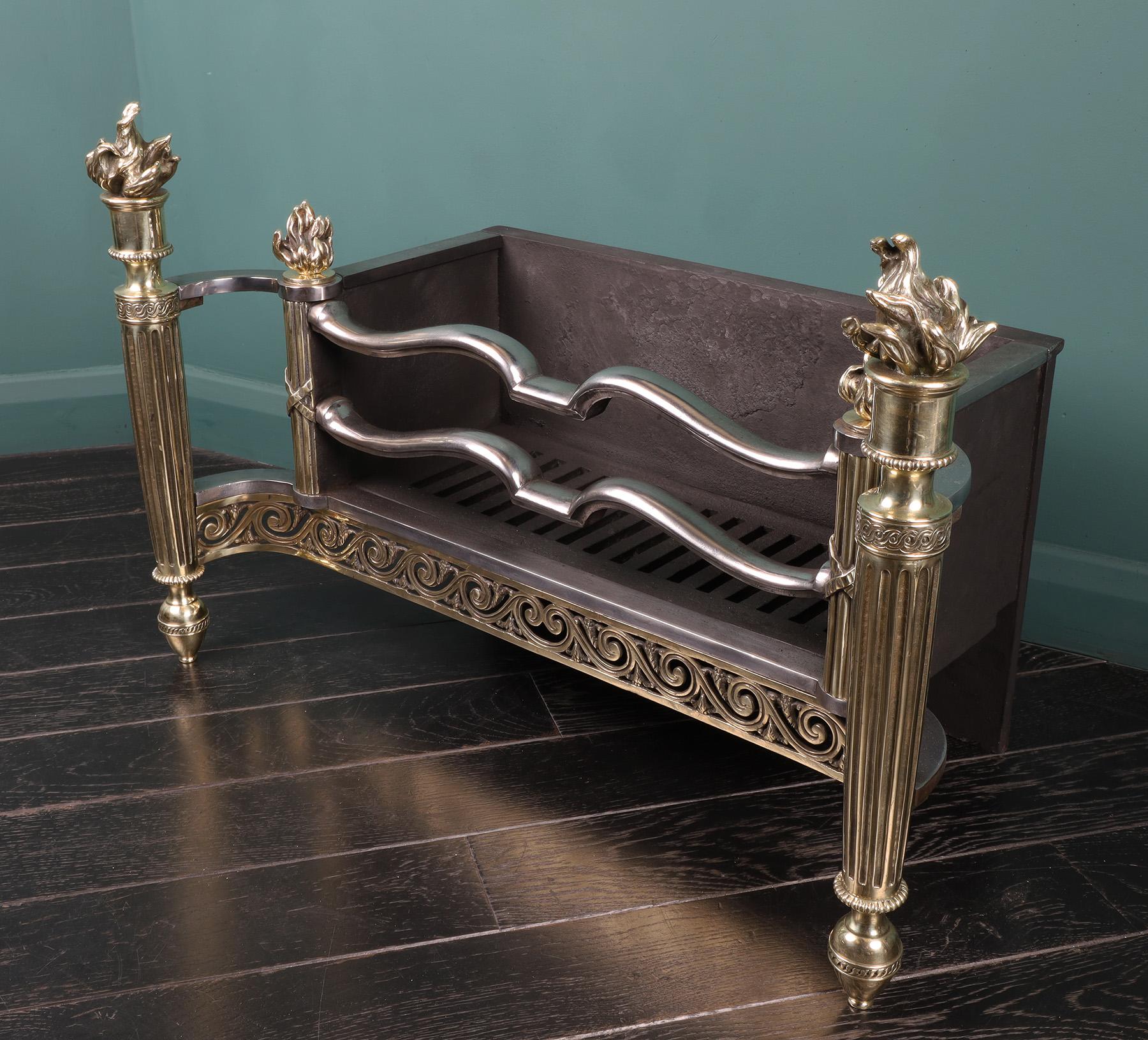 An English Brass and Steel fire grate in the Empire style. The rectangular fire basket with shaped polished steel fire bars flanked by brass reeded-column standards on urn feet with torch and flame finials uppermost. Restored.

Width at rear: 22