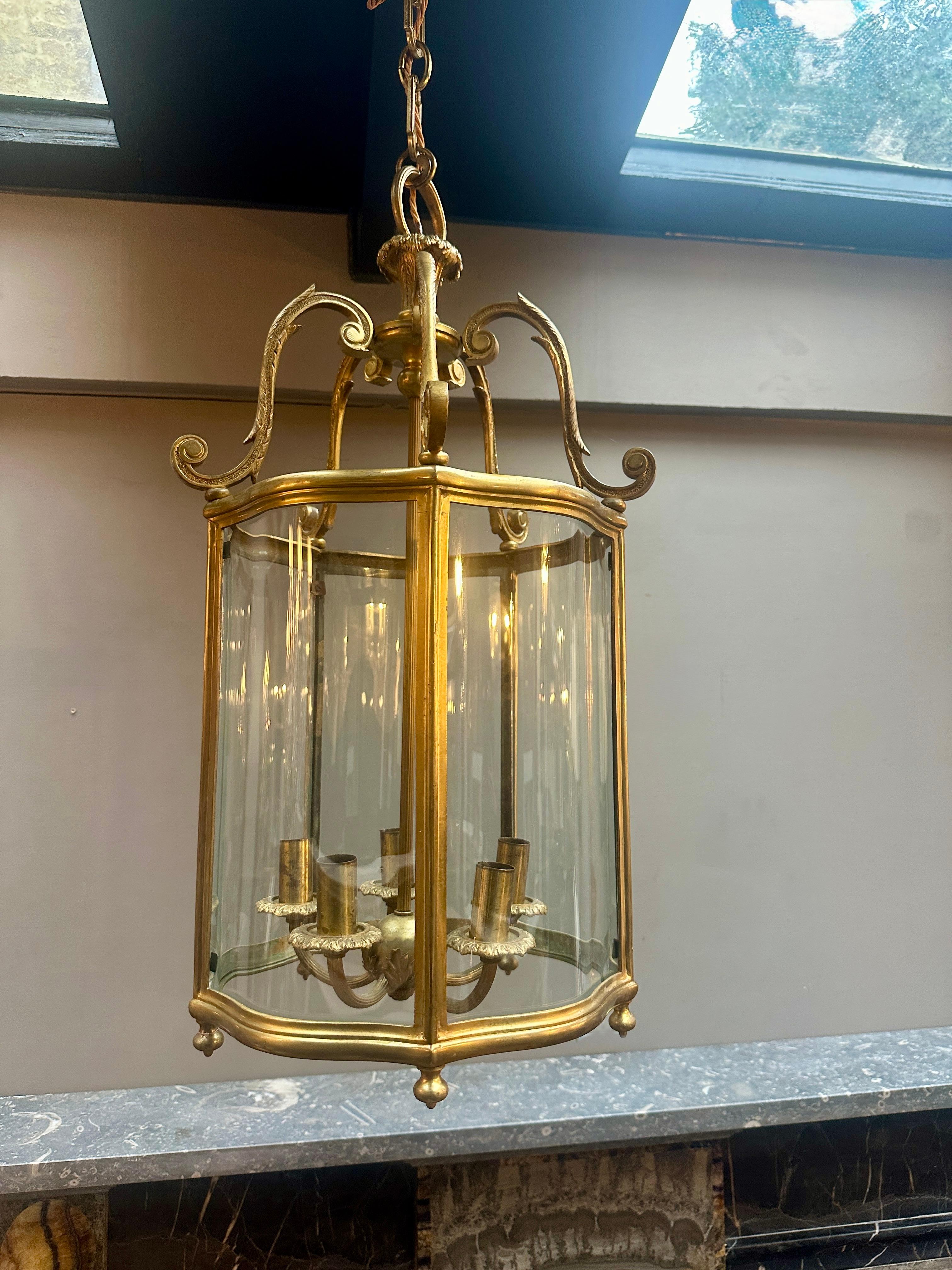 Lanterne anglaise ancienne en bronze, avec des panneaux de verre façonnés et incurvés. Le baldaquin est composé d'armoiries à feuillage et ciselé, avec un sommet à feuilles d'acanthe et des fleurons à la base. La branche à cinq bras est soutenue par
