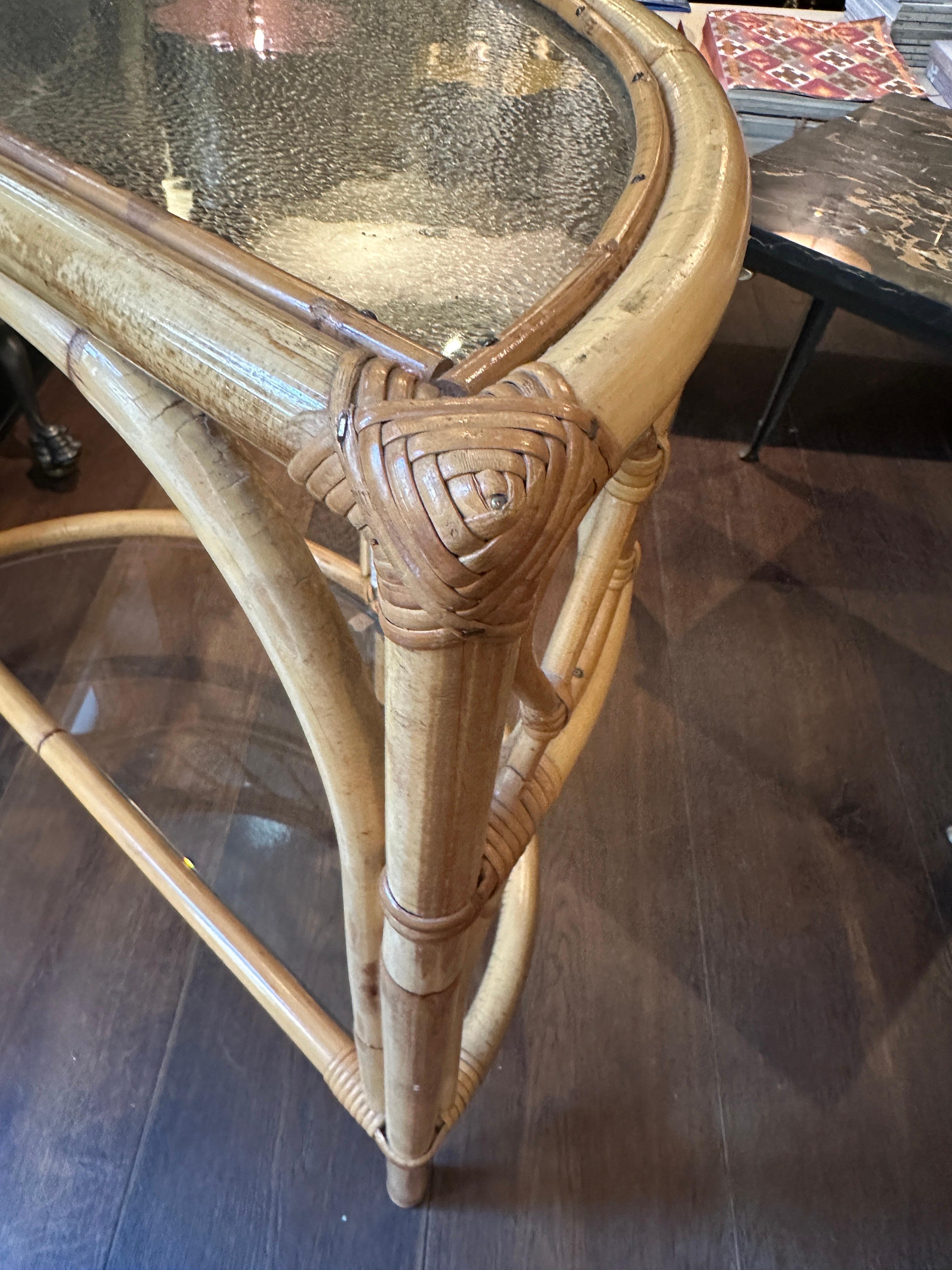 A small demi lune two tiered console table in cane or bamboo with rattan. The top glass plate in mottled frosted finish the bottom piece clear. Decorative border pateren. Very usable piece of furniture with a touch of the Riviera. By Angraves