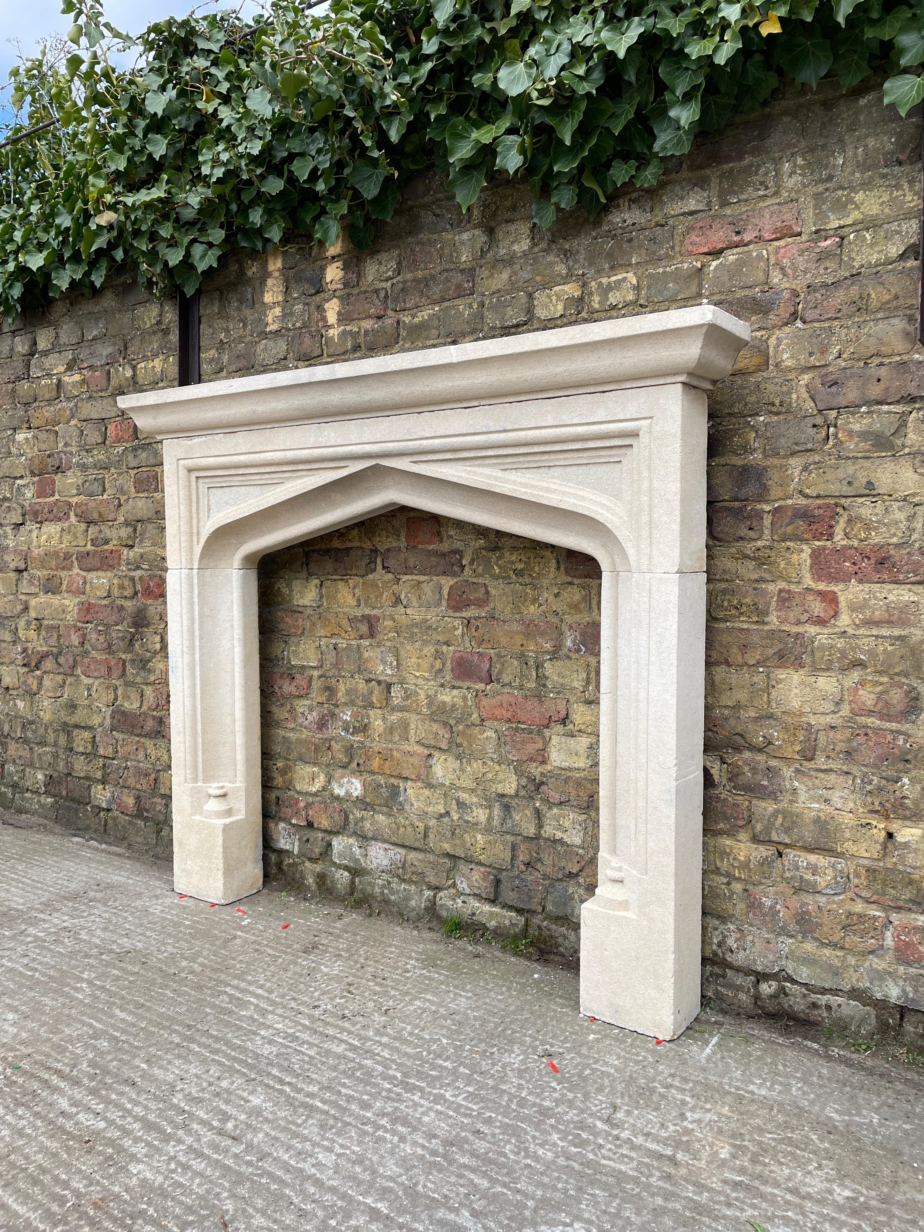 A Gothic style Bath stone fireplace, with carved panelled spandrels, moulded arched interior and jambs beneath a stepped and moulded shelf. English, 20th century.

Opening sizes:

96.5cm W x 96cm H.