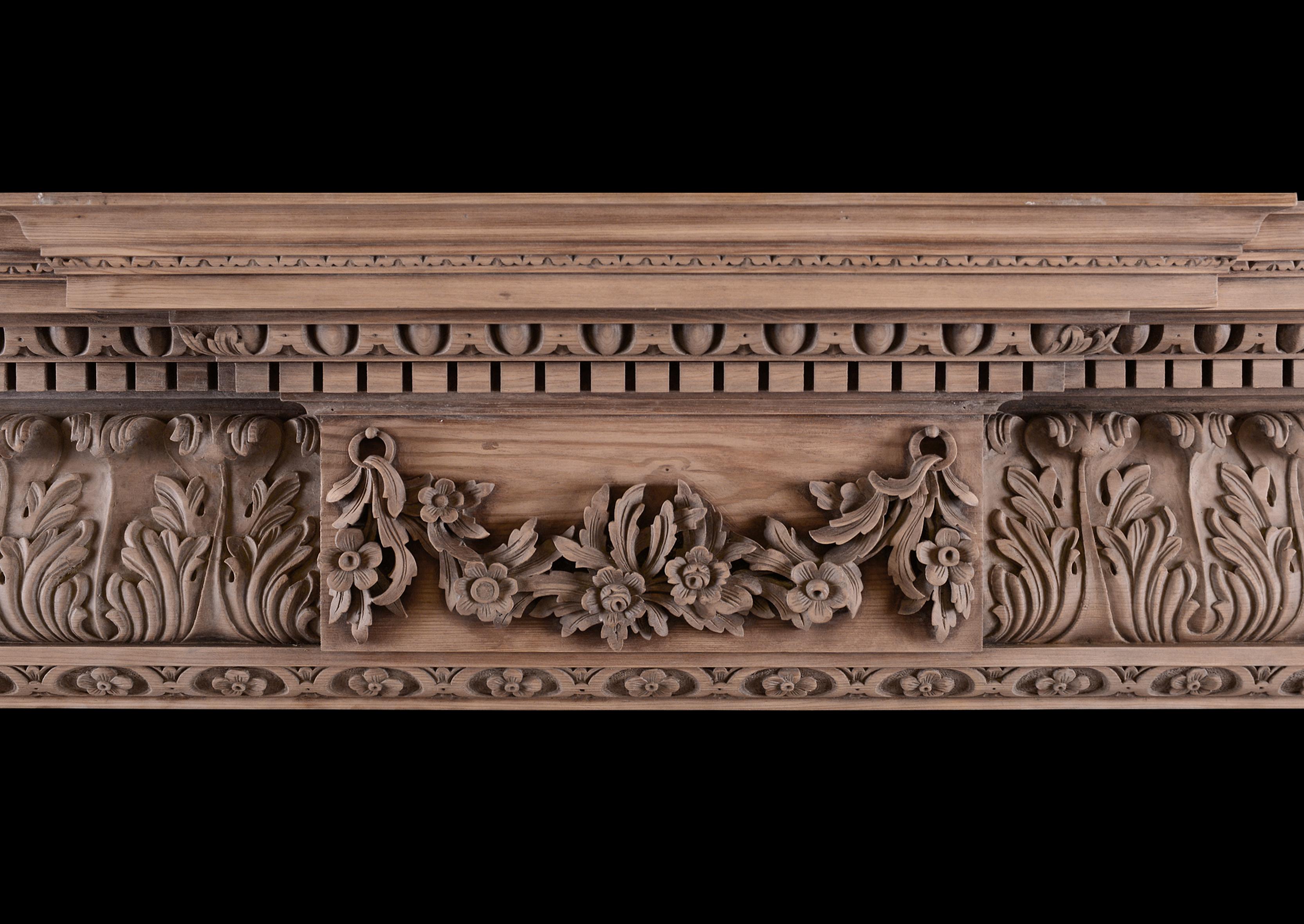 A carved pine fireplace in the Georgian manner. The break-leg jambs carved with flower petals, surmounted by acanthus leaf frieze with centre blocking featuring carved swags and flowers. The breakfront shelf with dentils and egg-and-tongue