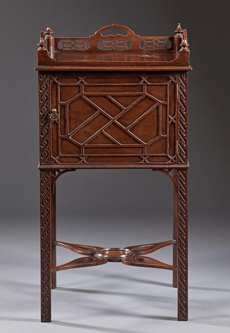 A Chinese Chippendale blind fretwork nightstand in mahogany having a pierced three sided gallery over a similarly traded single door compartment below and raised on square Marlborough legs with shaped cross stretcher and center turned disk. Probably