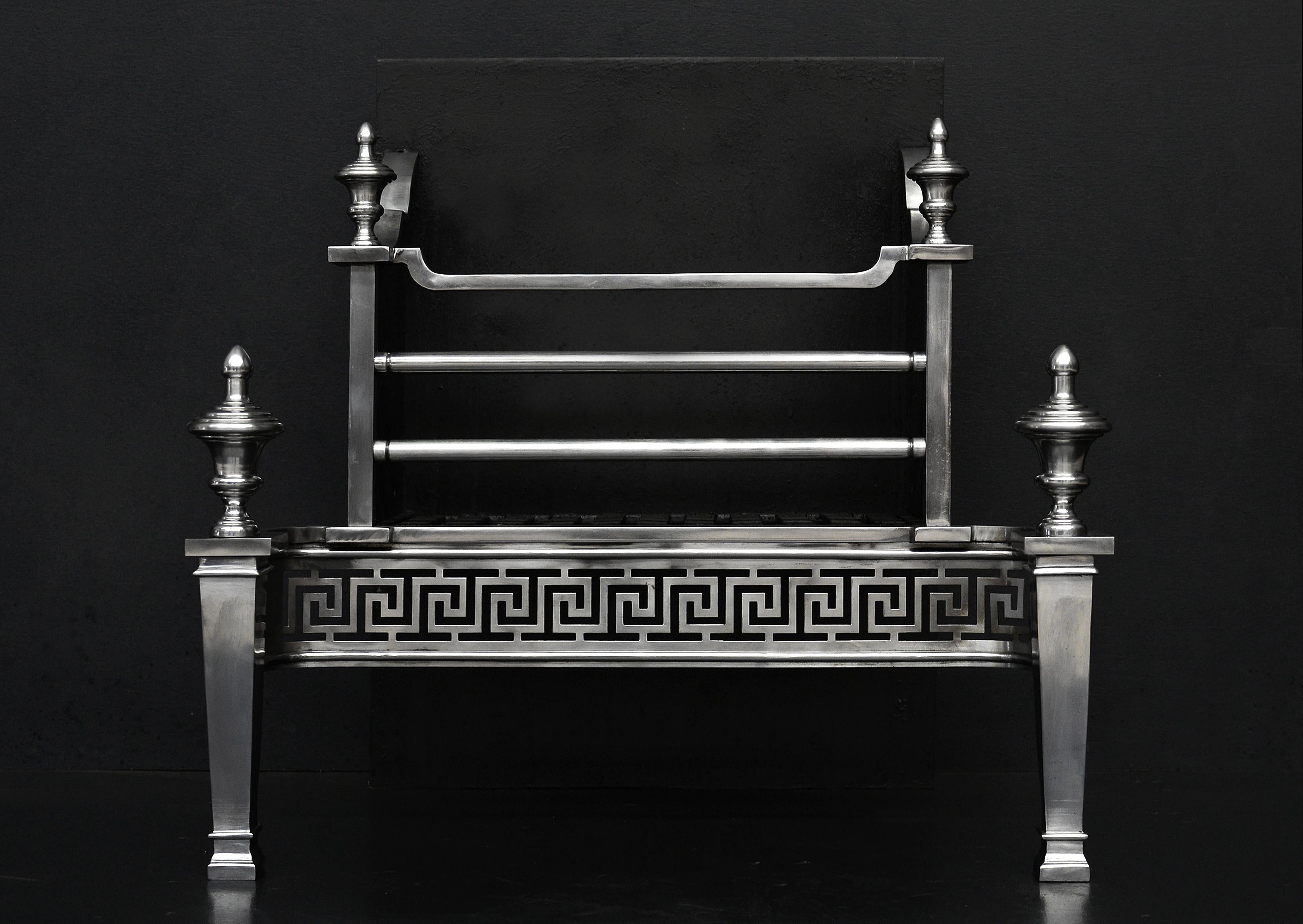An English firegrate in the Georgian style. The tapering legs surmounted by urn finials, the burning area with steel front bars and shaped top bar. Polished steel fret with Greek key motif throughout. Plain cast iron fireback behind.