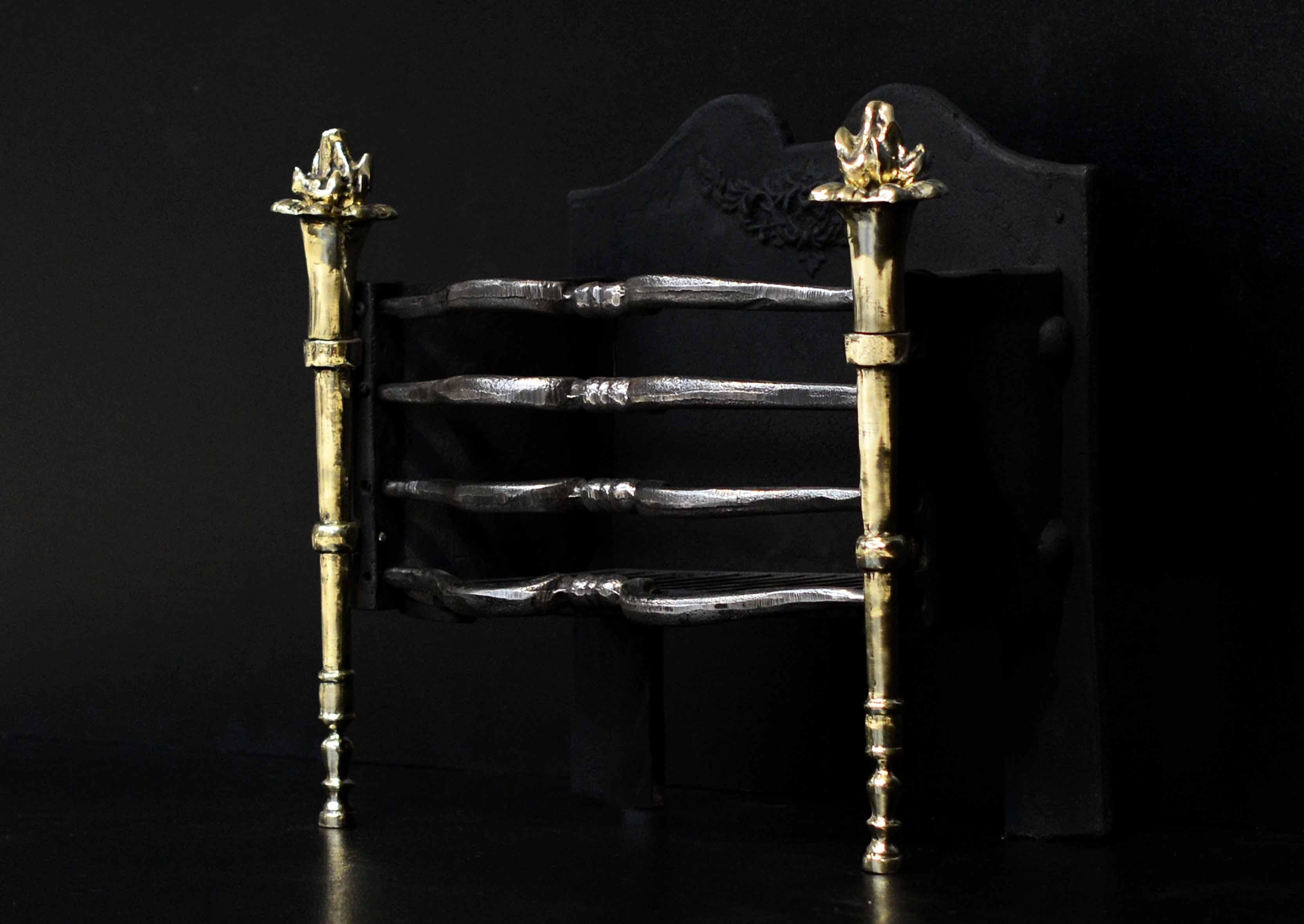 A compact English brass and steel firebasket. The shaped, polished cast iron front bars with tapering brass torch legs surmounted by flaming finials. Shaped cast iron back behind.

Width At Front:	505 mm      	19 ⅞
