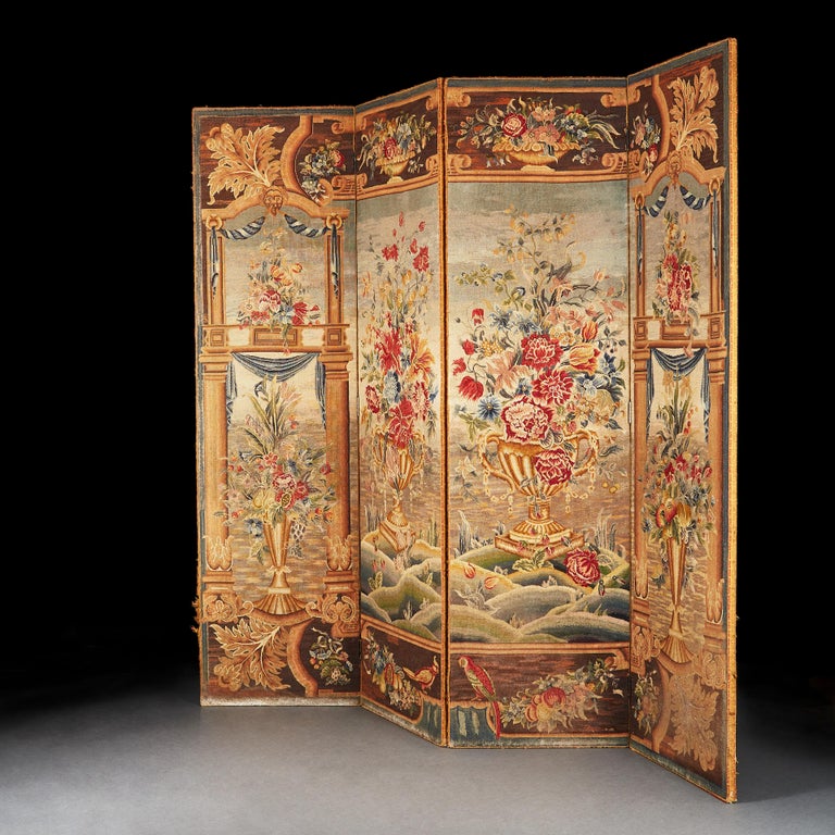 A four fold tapestry screen in the Flemish taste, each panel with flower arrangements standing in a landscape framed by architectural details. The outer edges with smaller floral arrangements, large acanthus leaves and a variety of birds.

Each