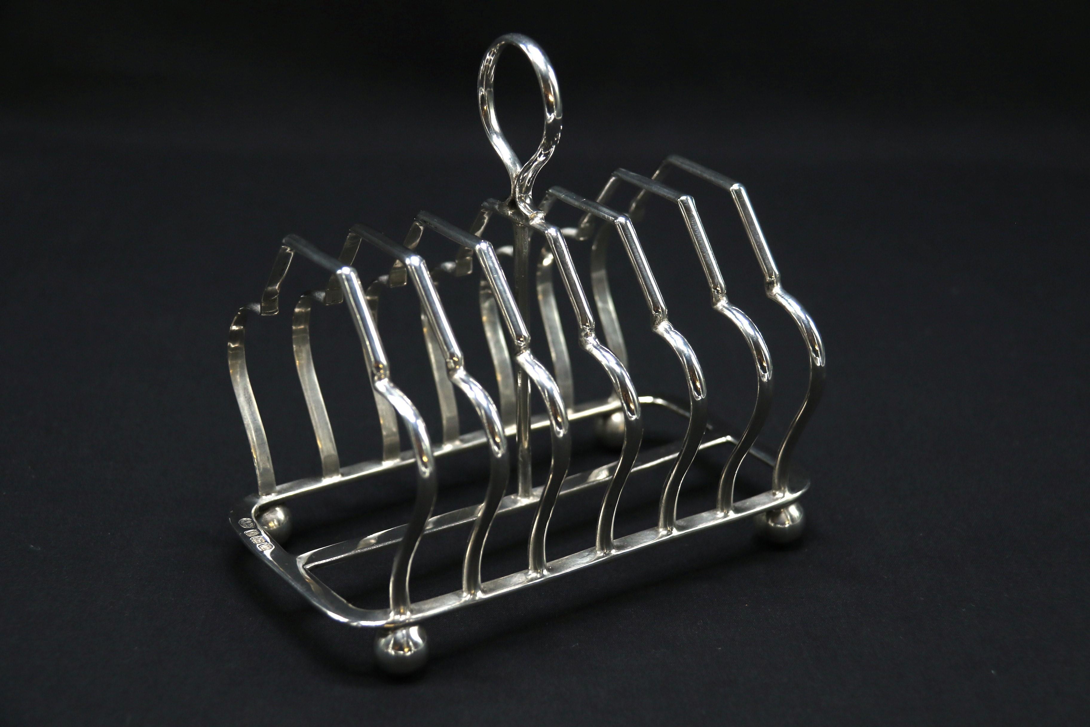 This fine English solid silver toast rack is elegant and of good practical proportions with a strong substantial construction. It stands on four ball feet which support the lower frame from which there are seven upright shaped divisions. The central