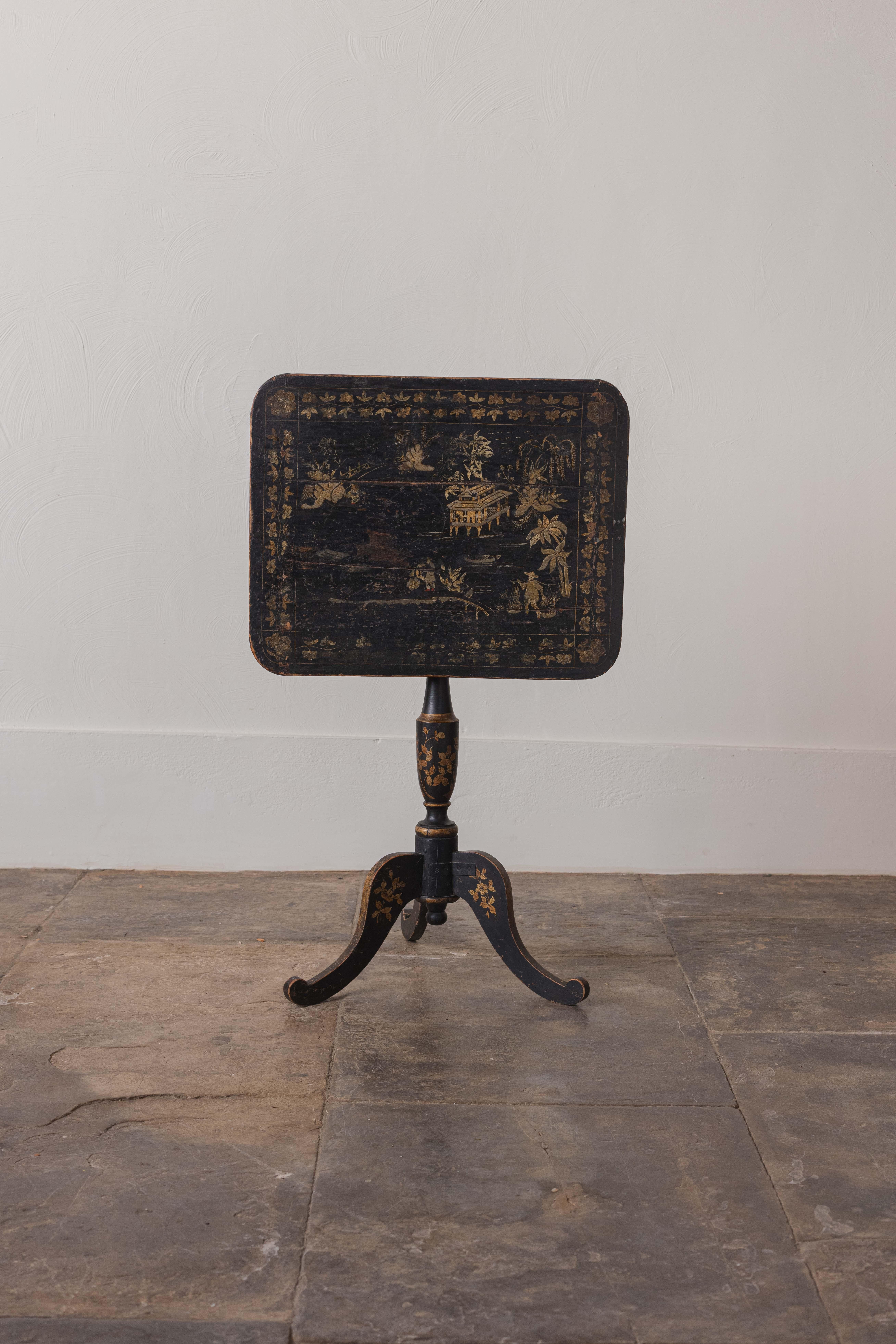 A Japanned chinoiserie tripod tilt-top table decorated in gilt with chinoiserie scenes on a black background. Made from wood with a turned central column and three splayed legs. A wonderful example of a late Regency oriental piece of furniture. Some